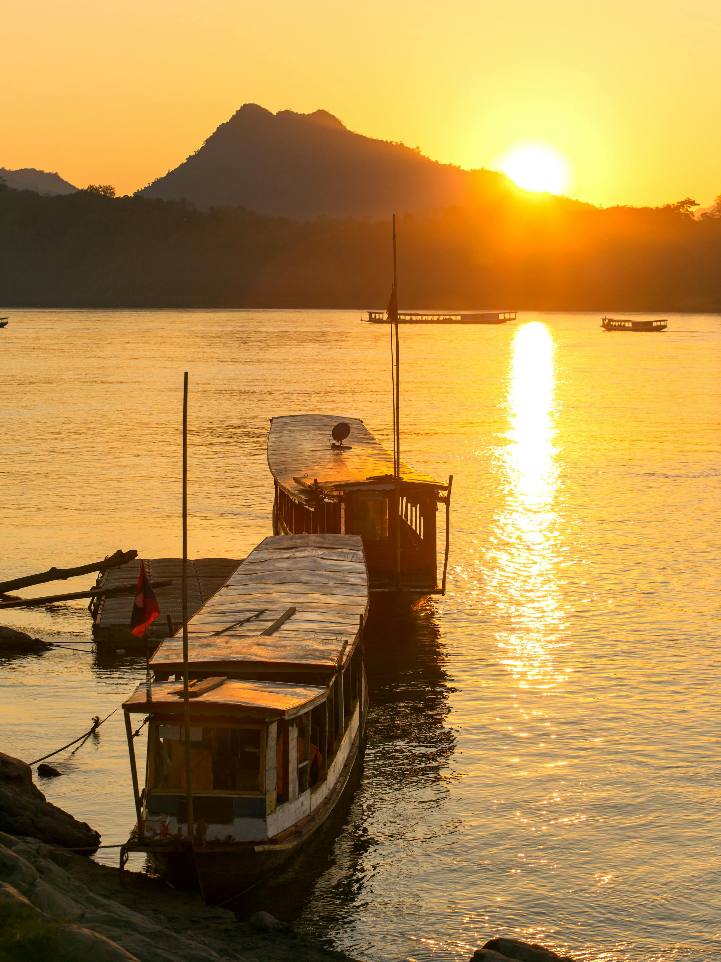 Wooden boat sits at a riverside dock at sunset, with golden light reflecting across calm water at sunset