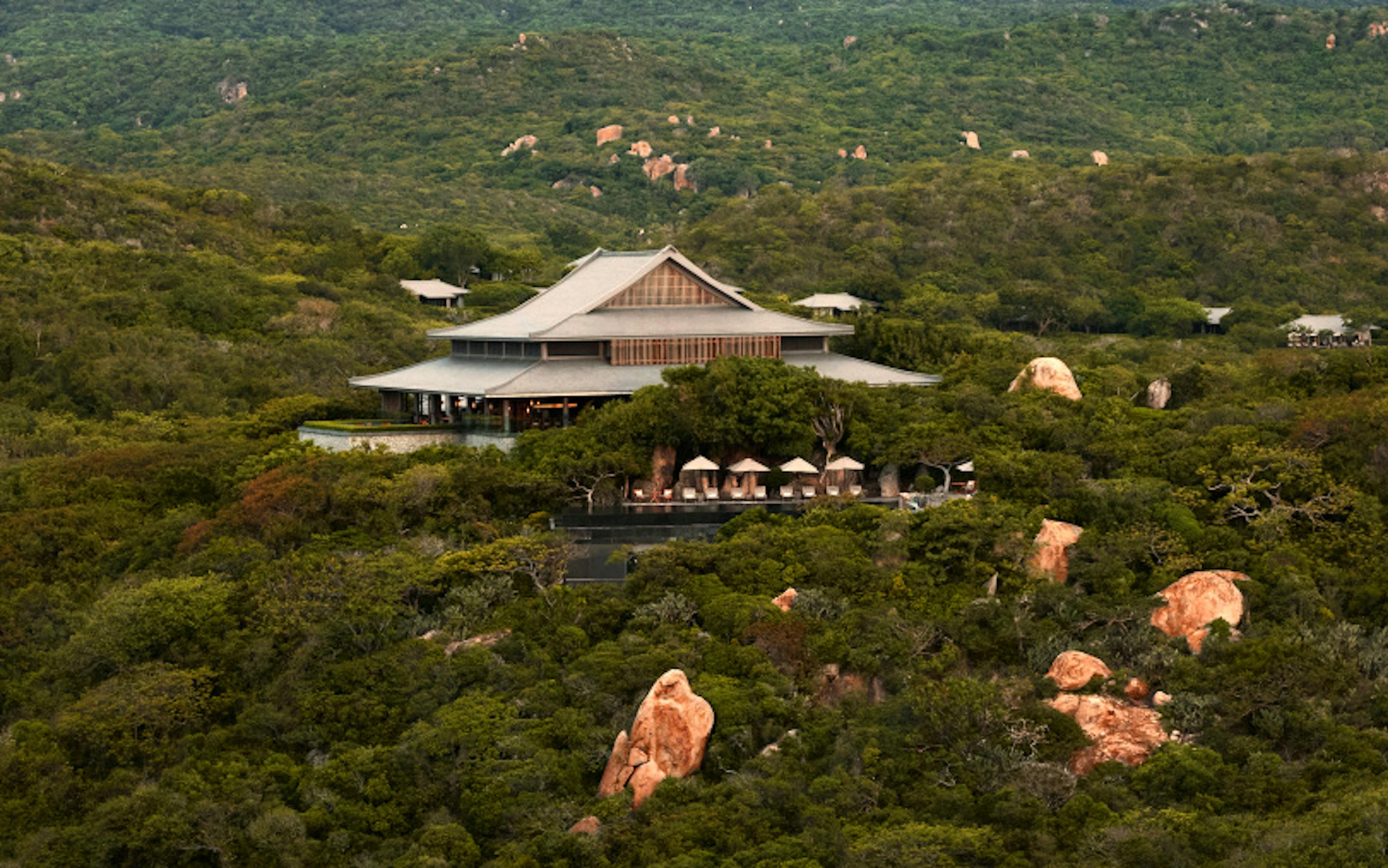 Resort buildings sit within dense green forest, with rooftops peeking above the canopy in soft haze under soft daylight.