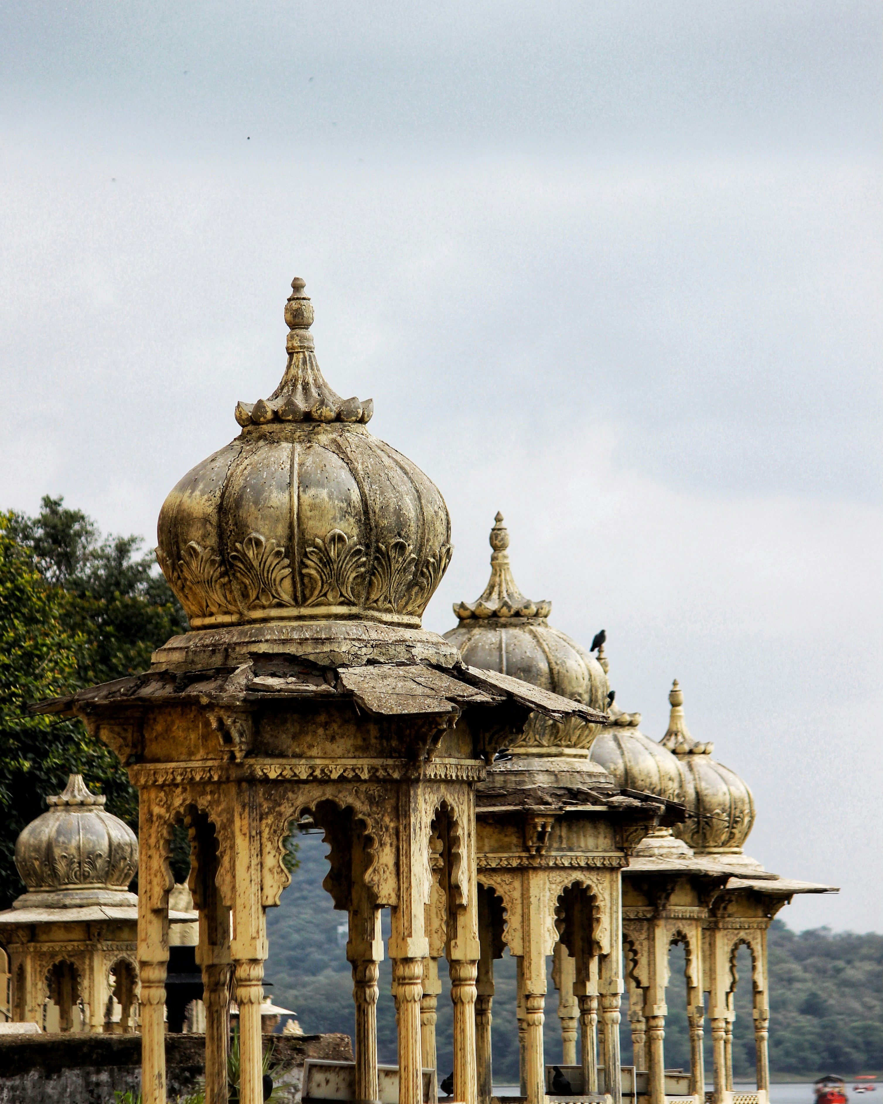 An ornate palace pavilion with domes and carved arches rises above weathered stone, set against a pale sky.