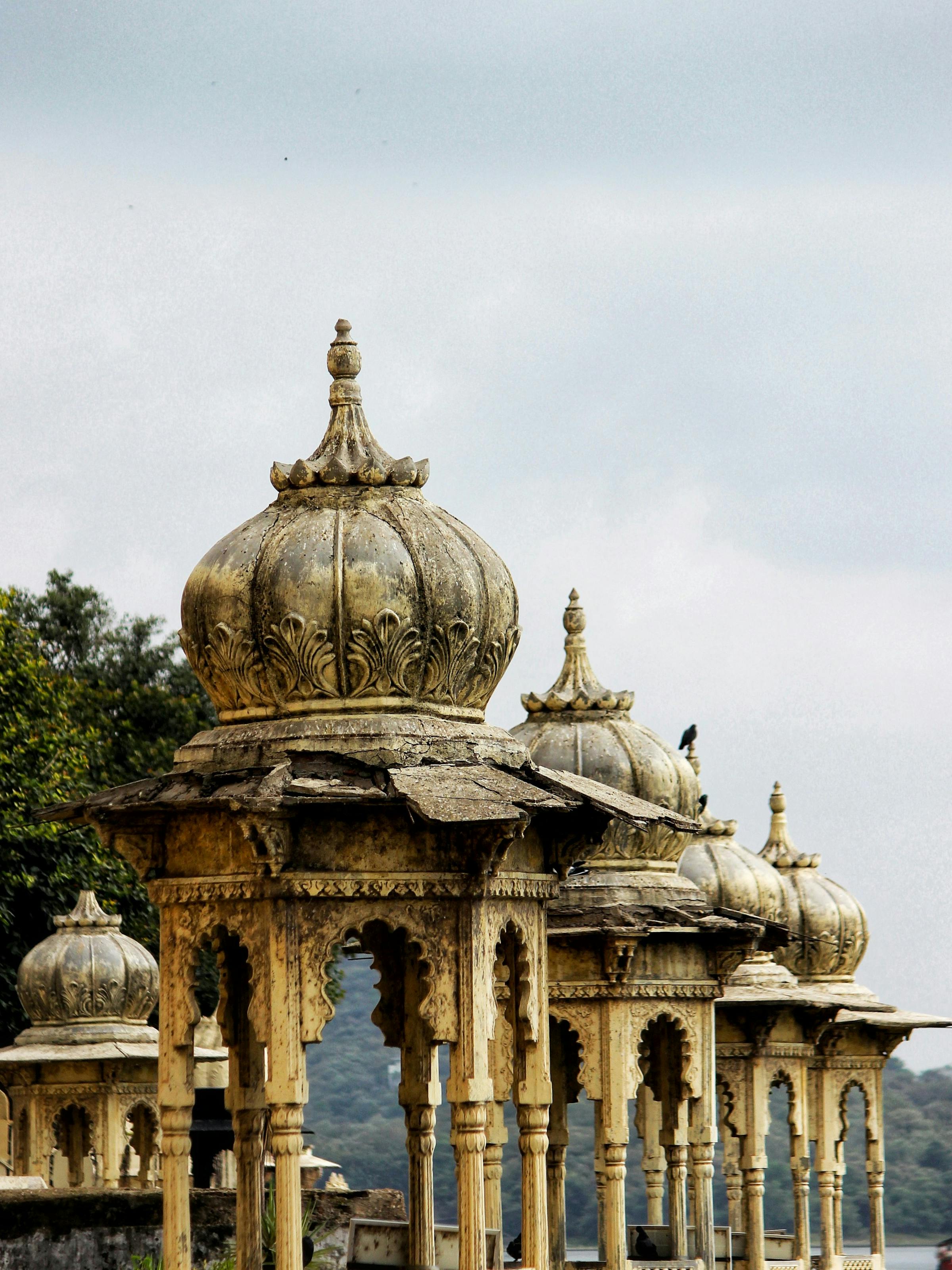 An ornate palace pavilion with domes and carved arches rises above weathered stone, set against a pale sky.
