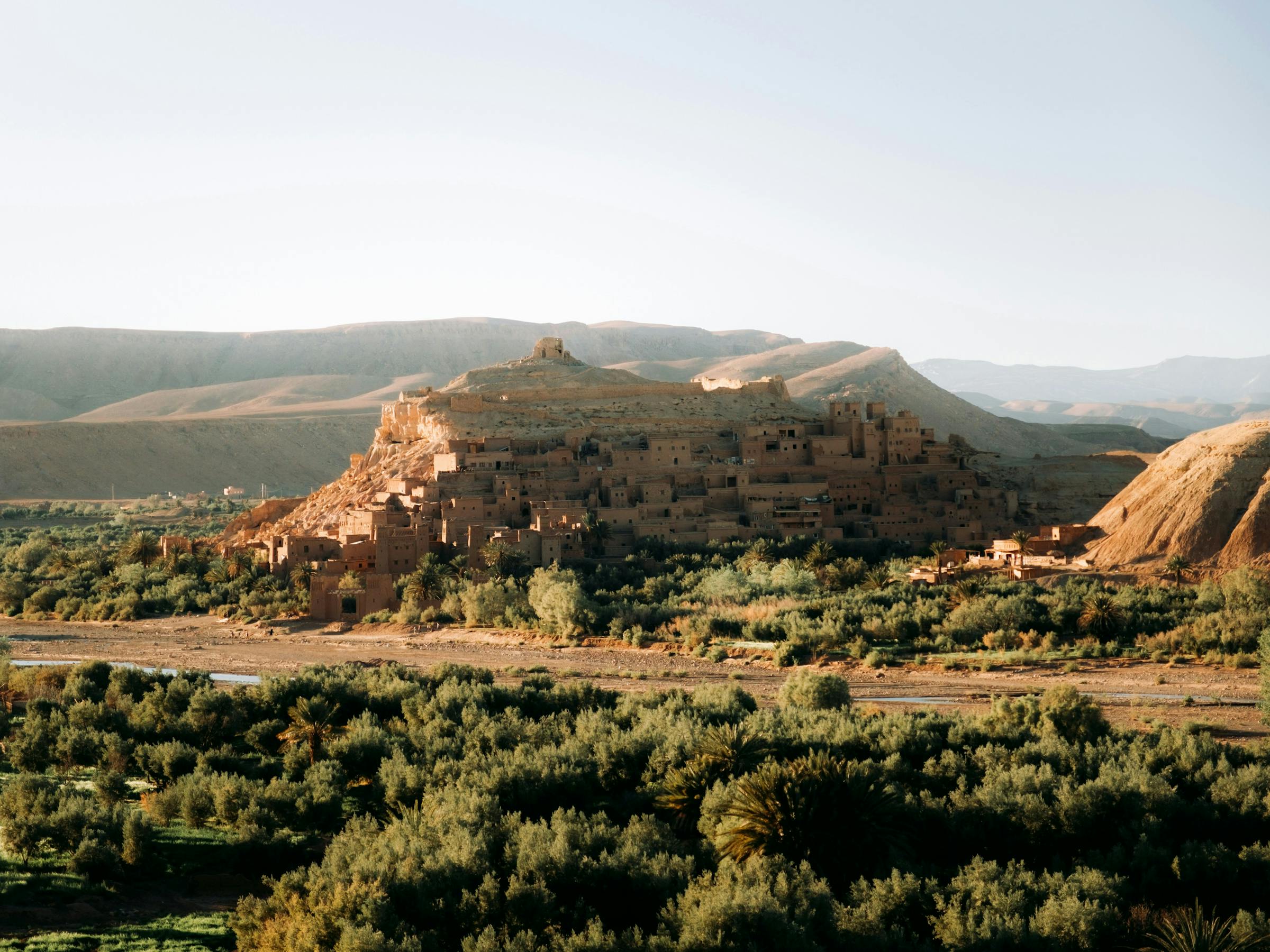 Wide green valley with scattered houses and terraced fields, framed by low hills and clear evening light.