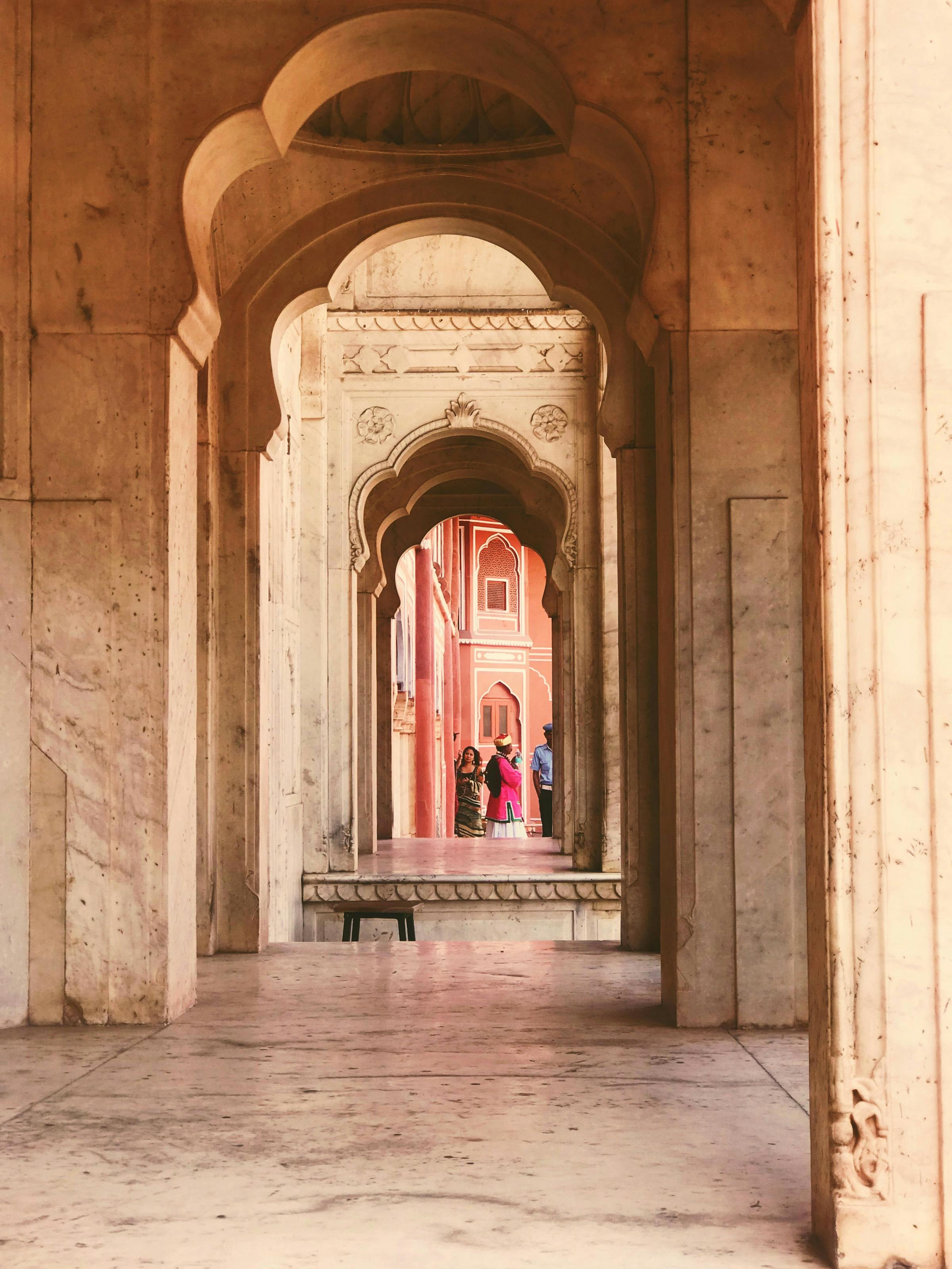 A long arched hallway recedes into the distance, with patterned stone floors and a lone figure in the far doorway.