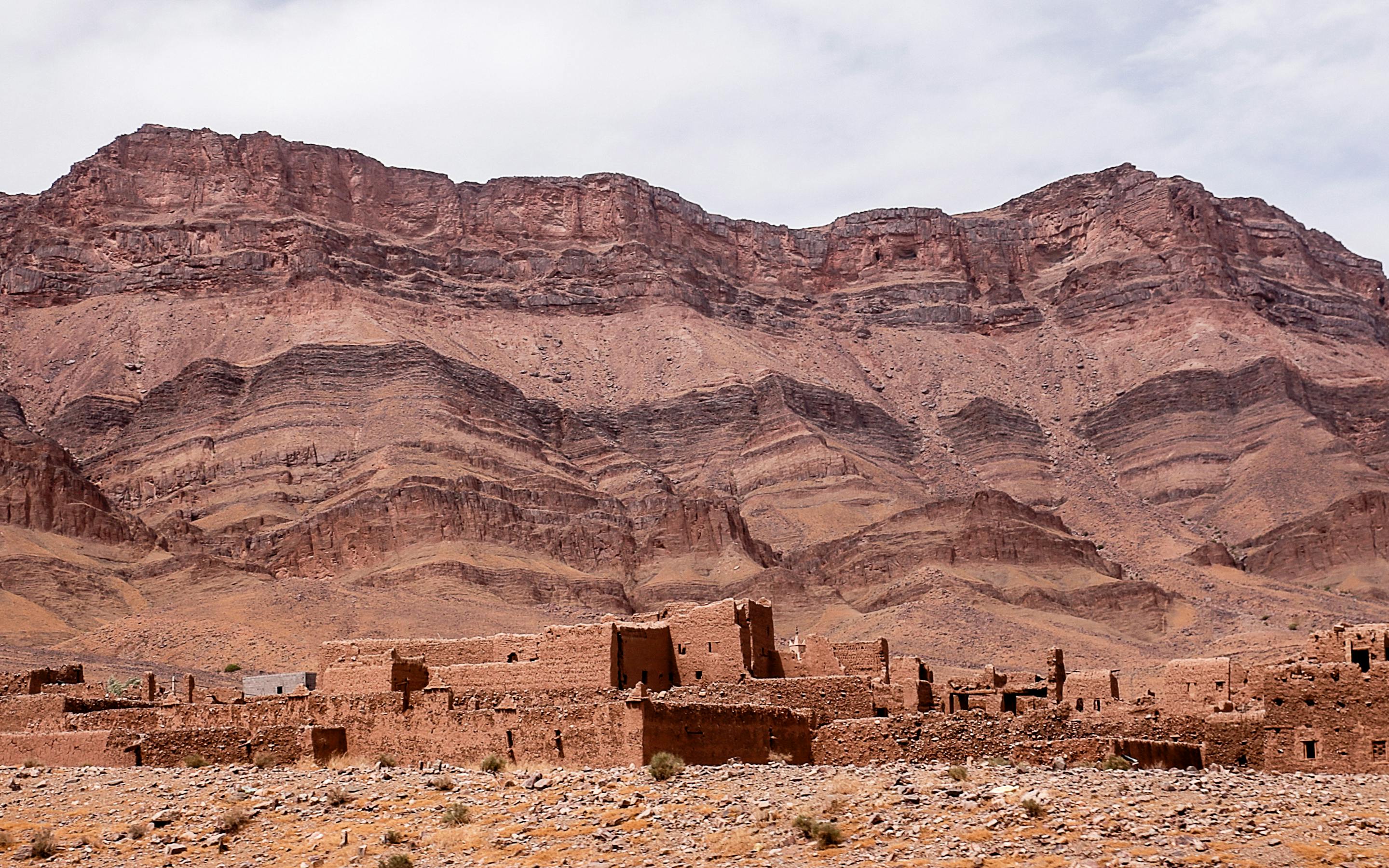 Layered desert mountains and dry plains stretch to the horizon, with a few stone ruins scattered in the foreground.