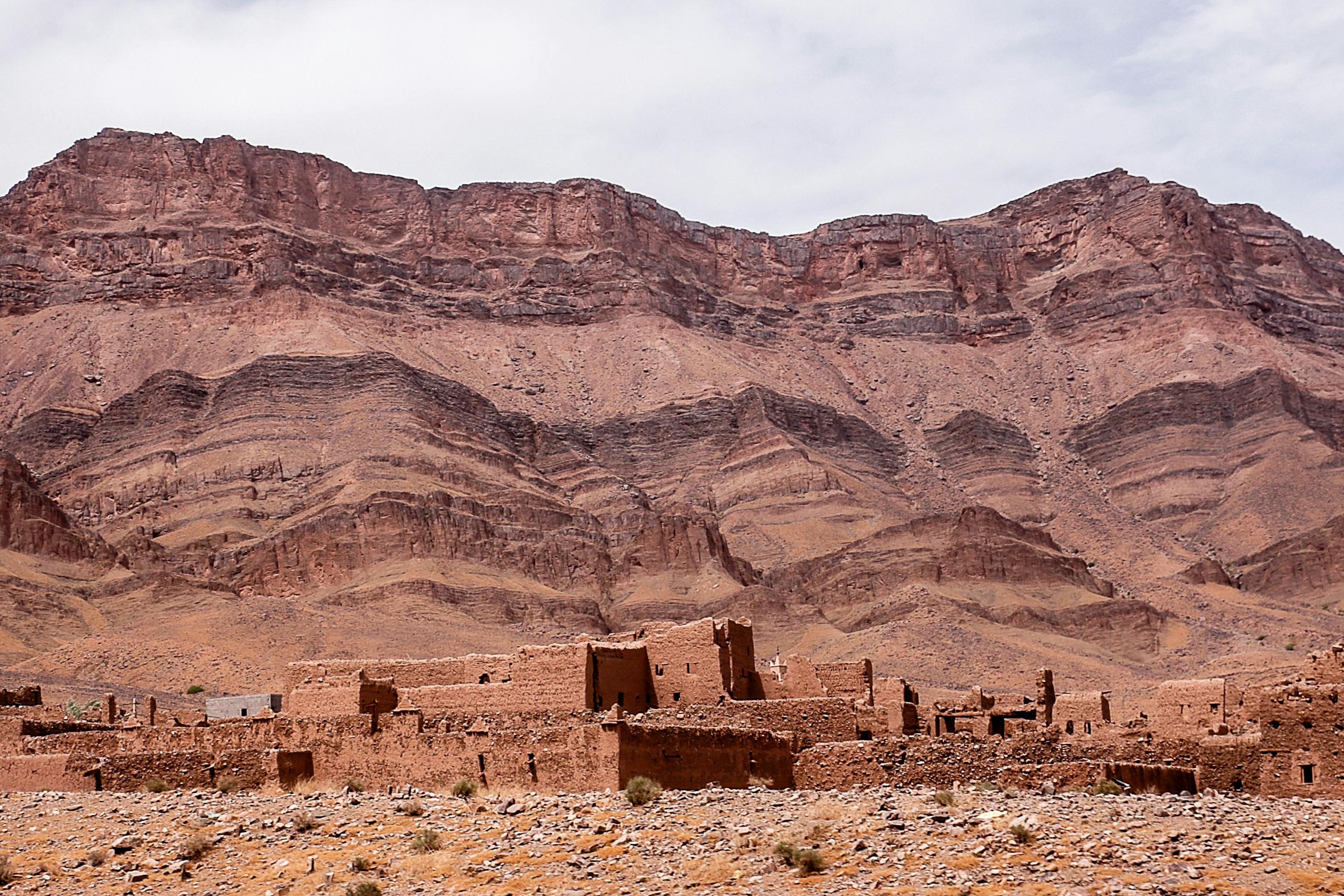 Layered desert mountains and dry plains stretch to the horizon, with a few stone ruins scattered in the foreground.