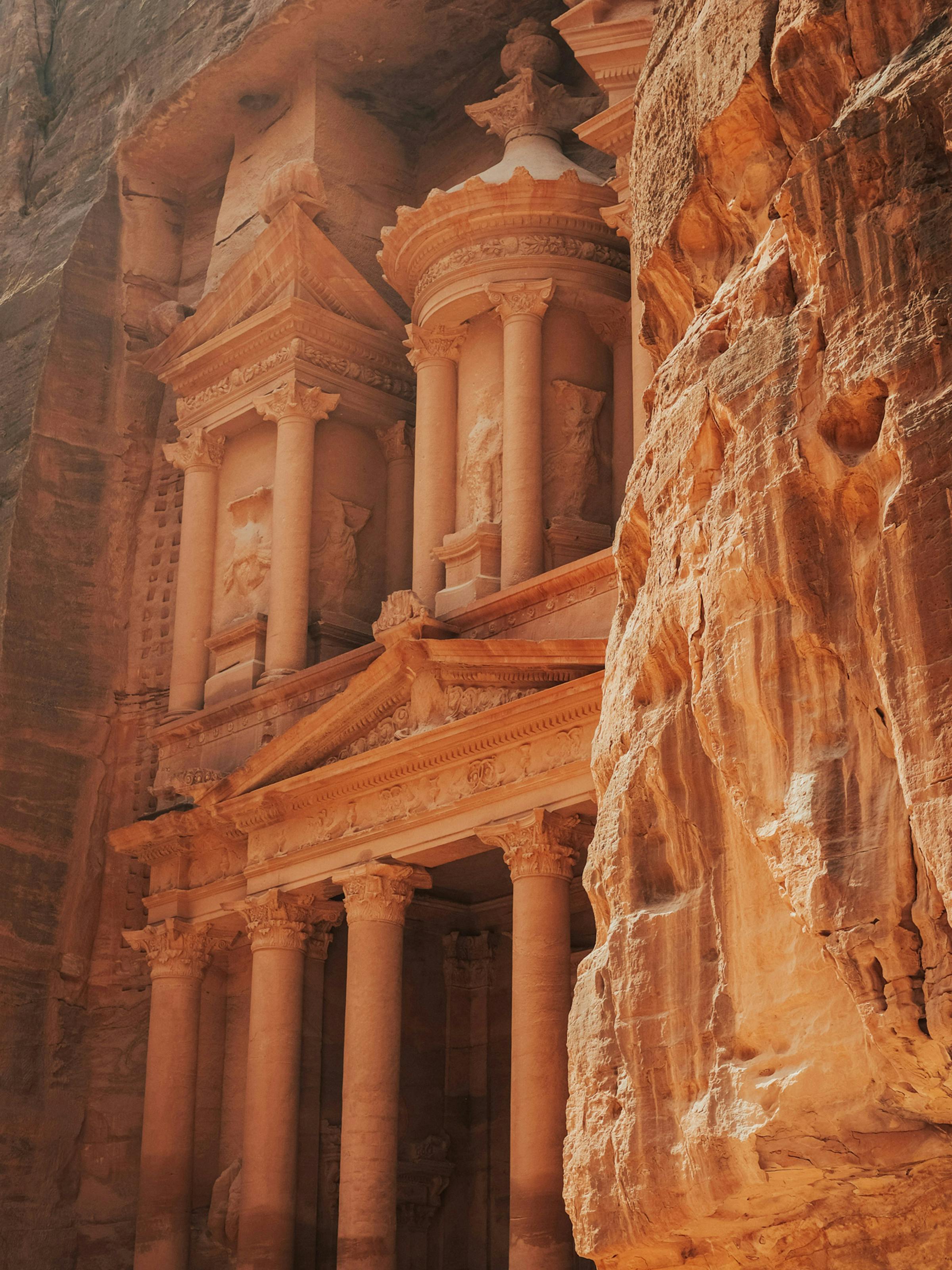 Rock-cut temple façade with columns and carvings emerges from a canyon wall, with warm sandstone textures.