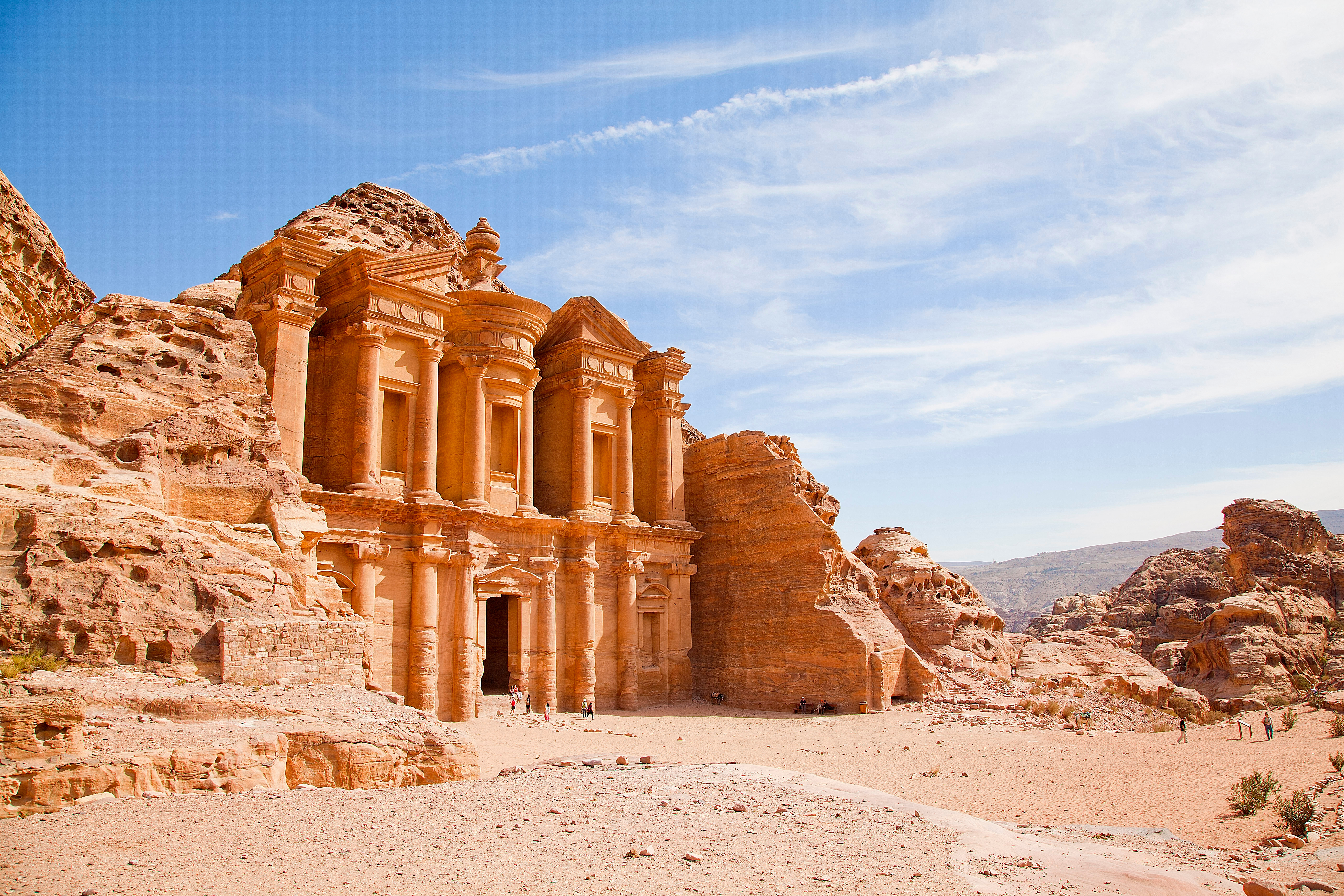Carved sandstone temple facade in a desert canyon under a blue sky.