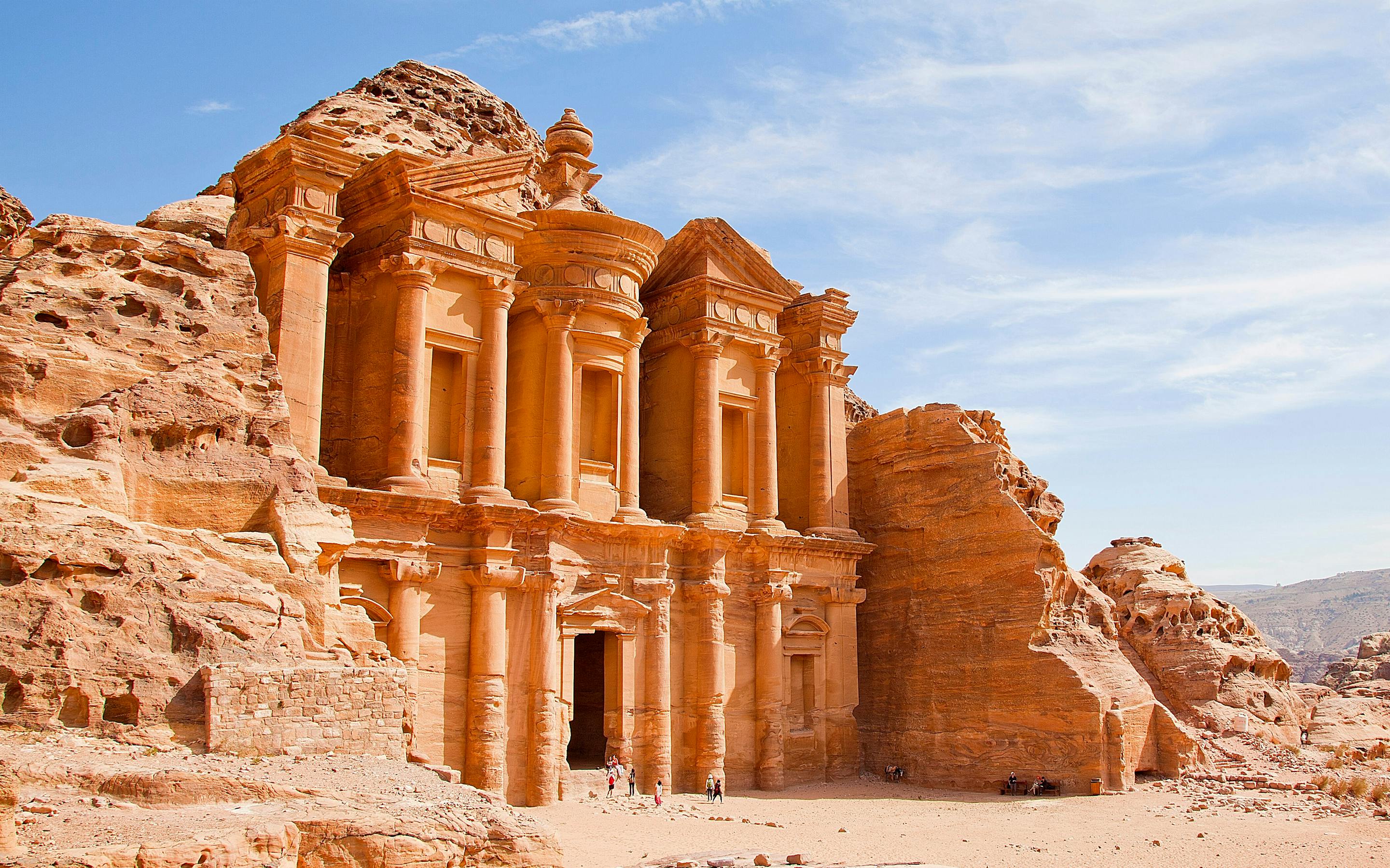 Carved sandstone temple facade in a desert canyon under a blue sky.