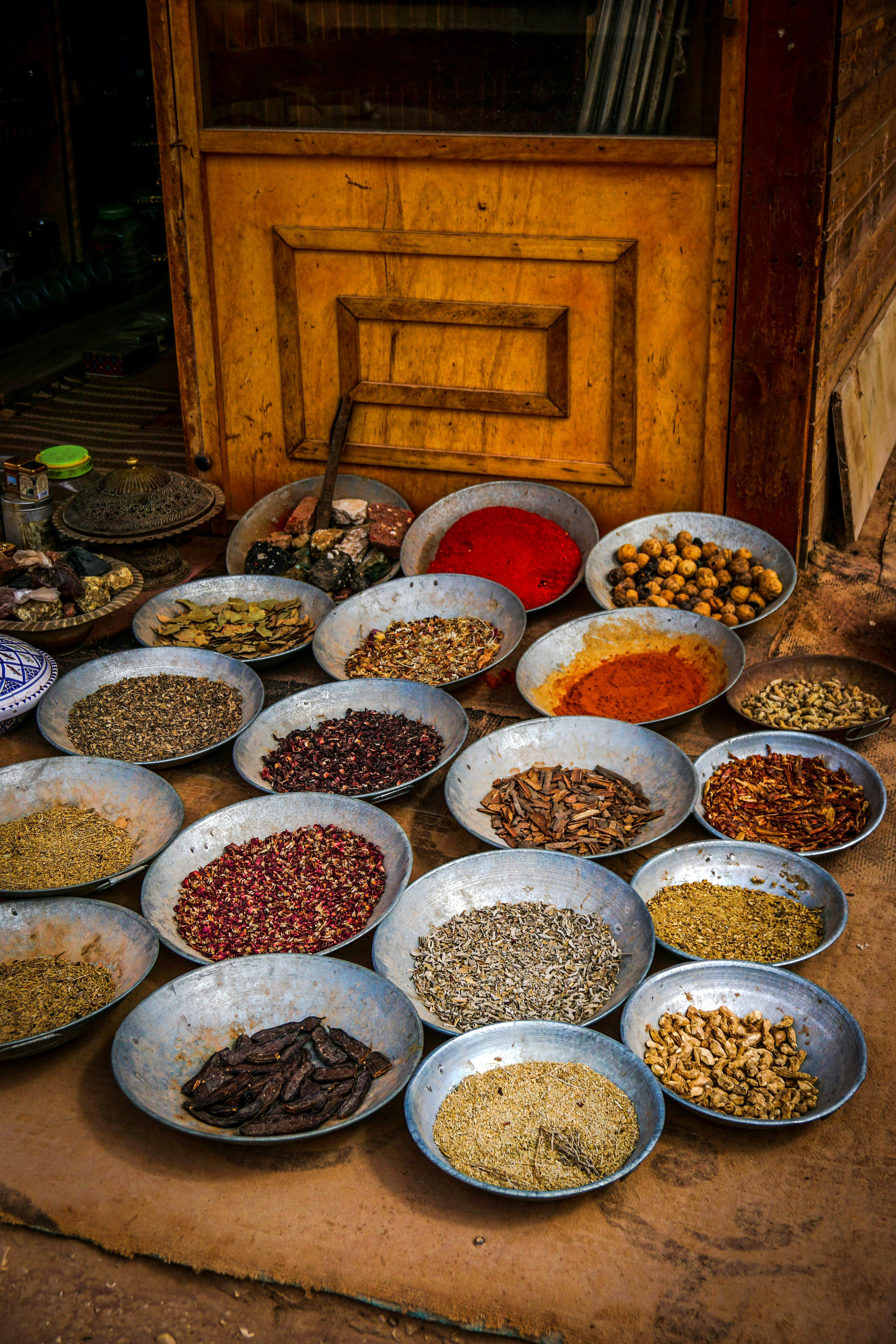 Bowls of colorful spices and grains arranged on the floor beside a wooden cabinet.