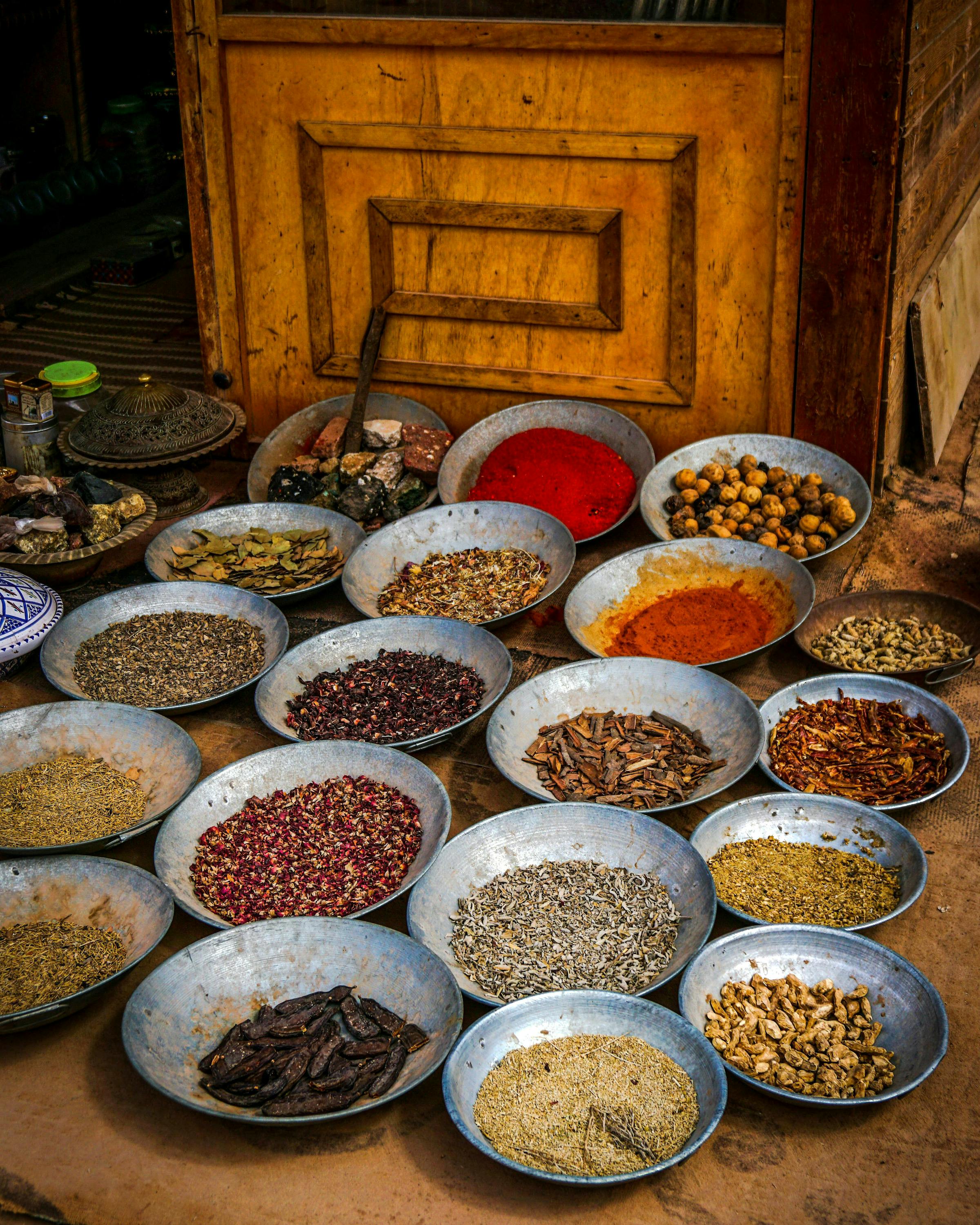 Bowls of colorful spices and grains arranged on the floor beside a wooden cabinet.