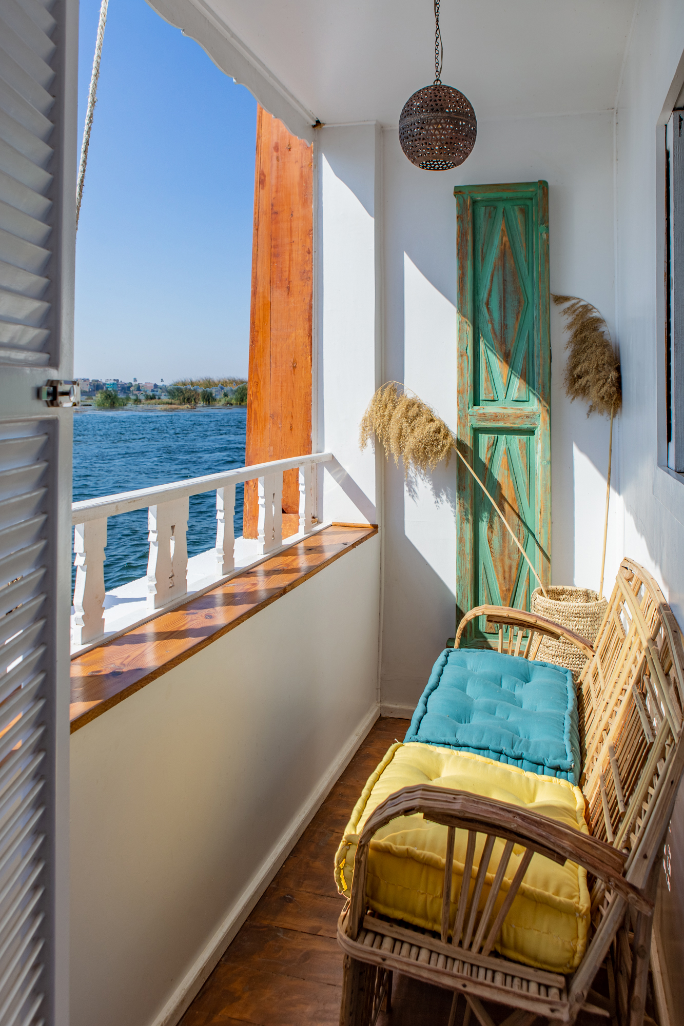 Private balcony with a wicker chair overlooks a wide river, with white railing and low green banks beyond.