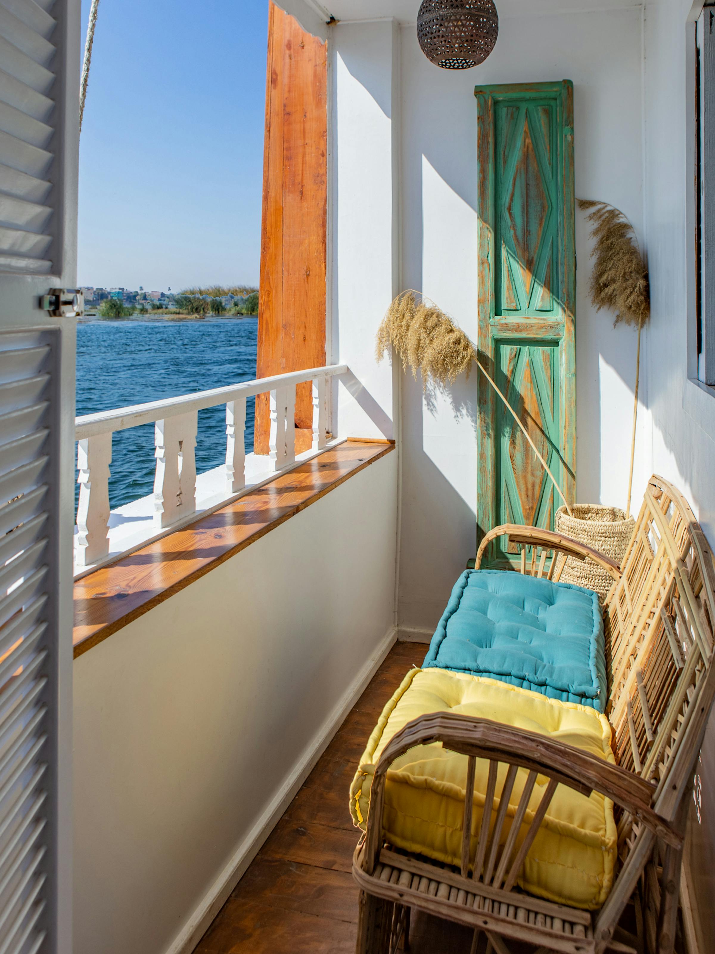 Private balcony with a wicker chair overlooks a wide river, with white railing and low green banks beyond.
