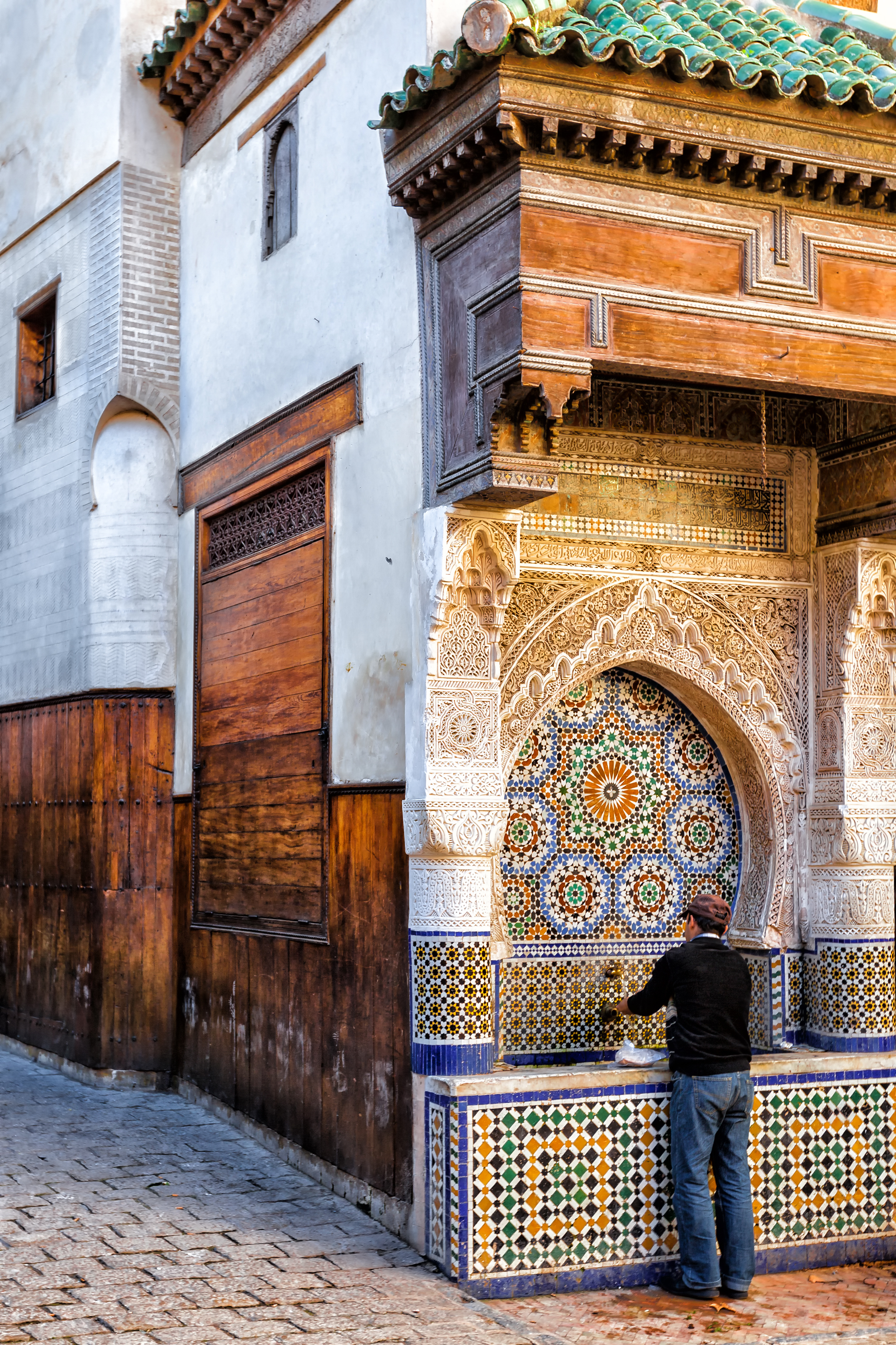 Blue-and-white tiled doorway and wooden doors in a narrow street, with carved plaster and mosaic details.