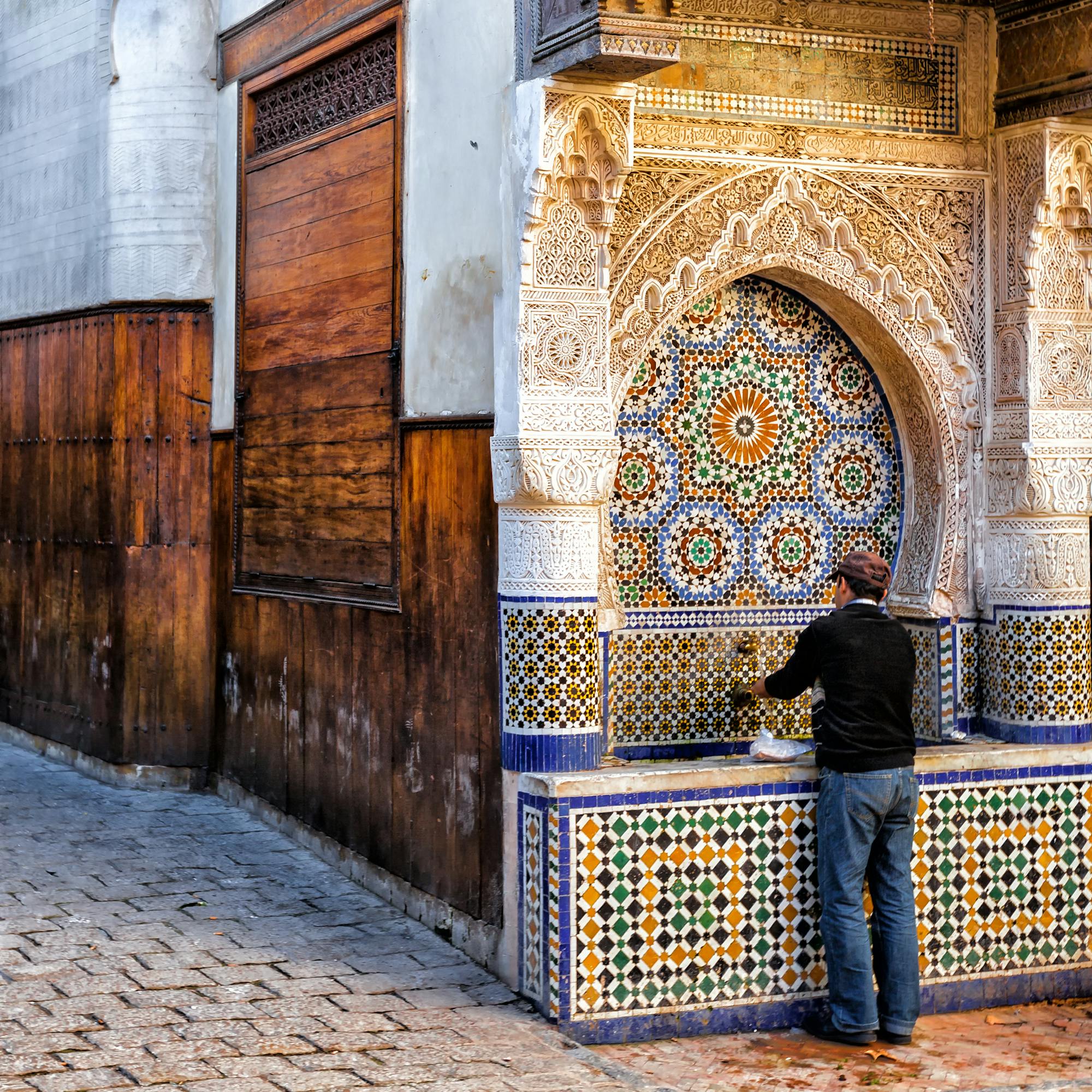 Blue-and-white tiled doorway and wooden doors in a narrow street, with carved plaster and mosaic details.