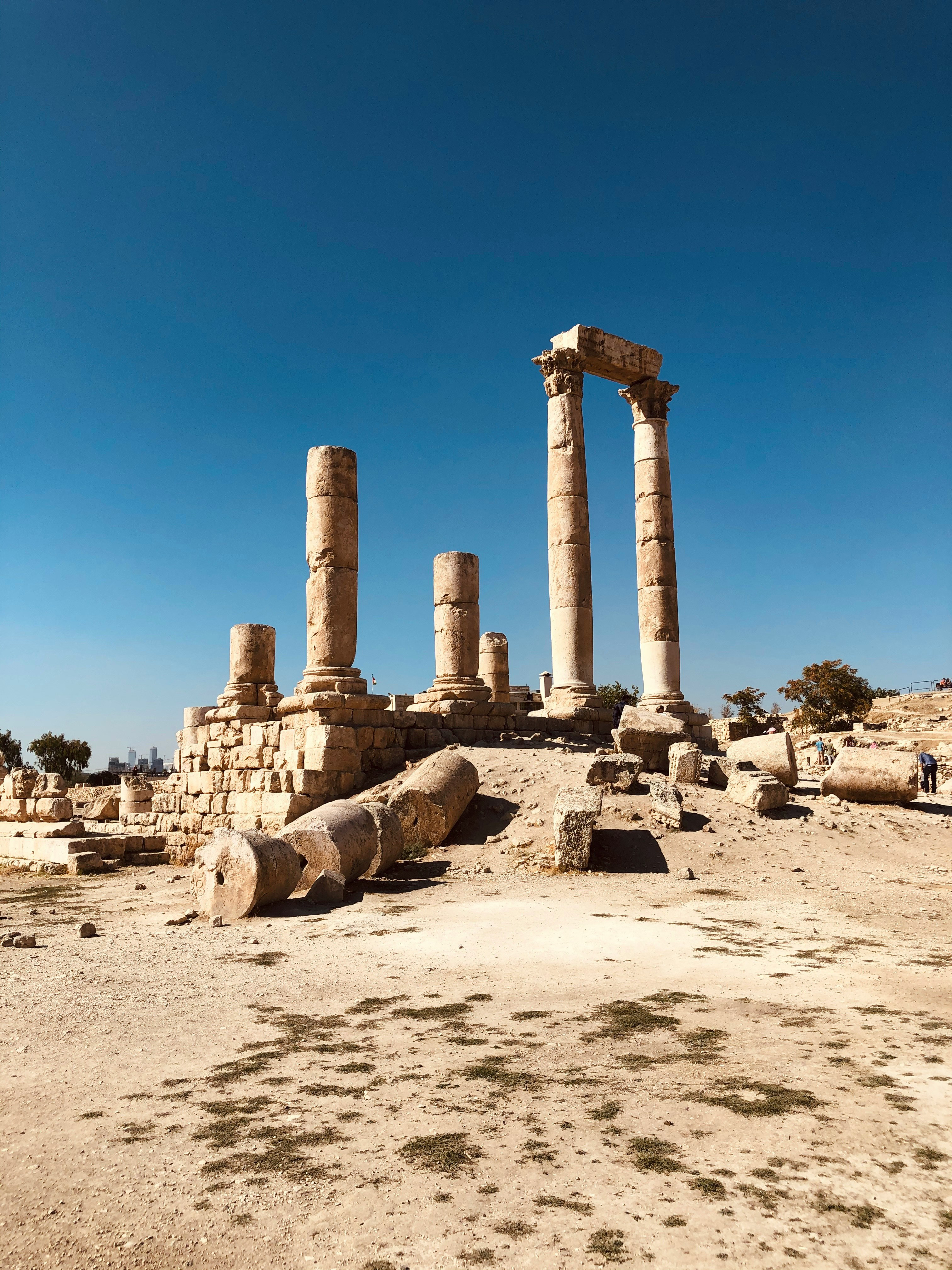 Ancient stone columns rise from a sandy site, with scattered blocks at their base and a deep blue sky overhead.