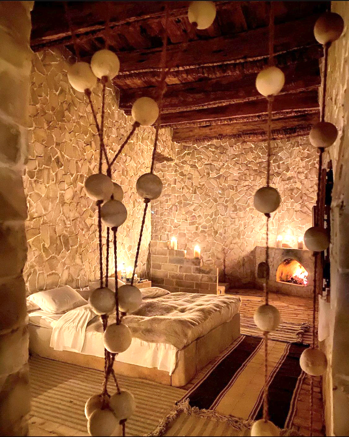 Warmly lit rustic bedroom with wooden beams, hanging lamps, and natural decor.
