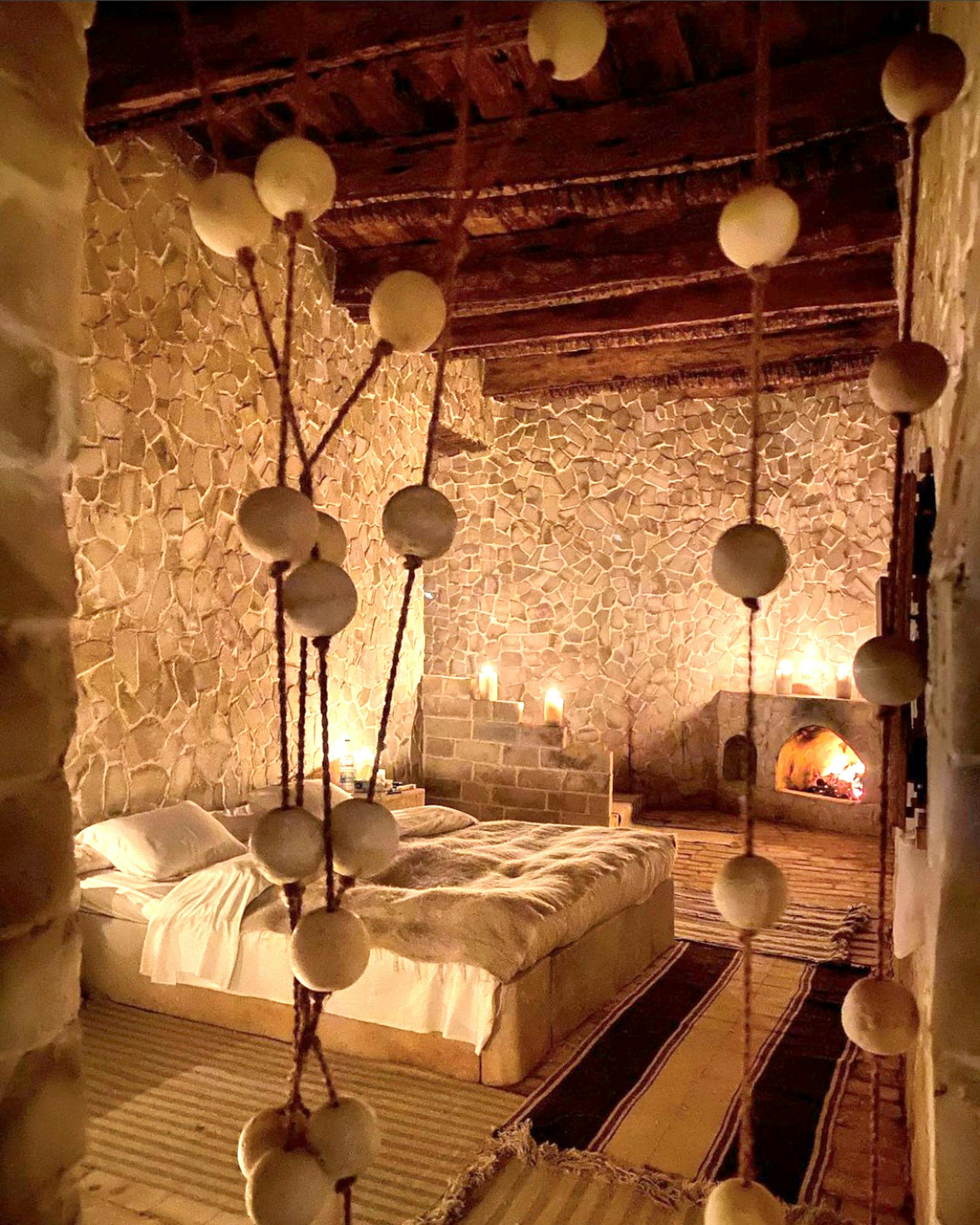 Warmly lit rustic bedroom with wooden beams, hanging lamps, and natural decor.
