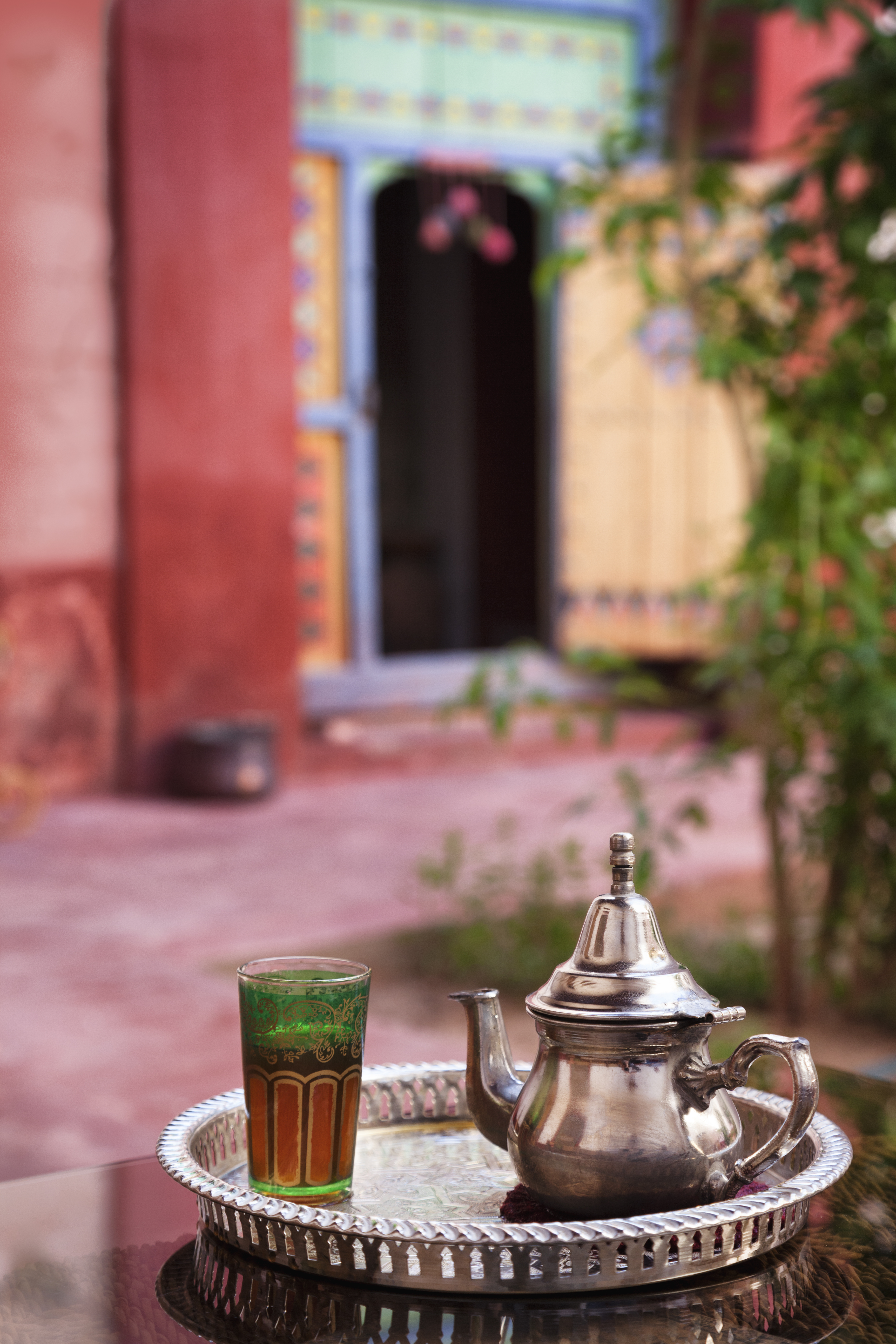 Silver teapot and tea glass on a tray near a colorful doorway.