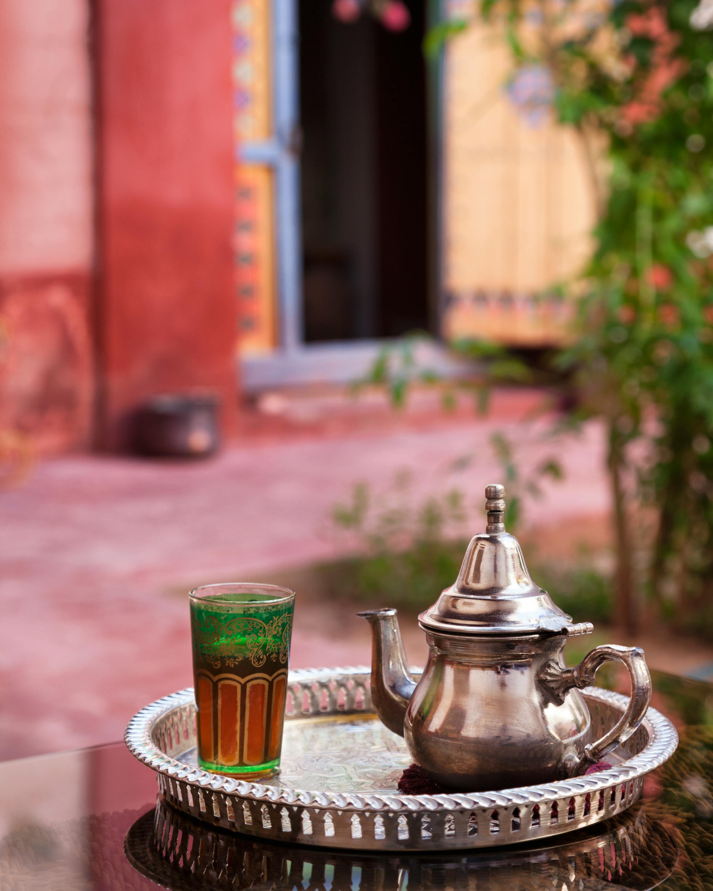 Silver teapot and tea glass on a tray near a colorful doorway.