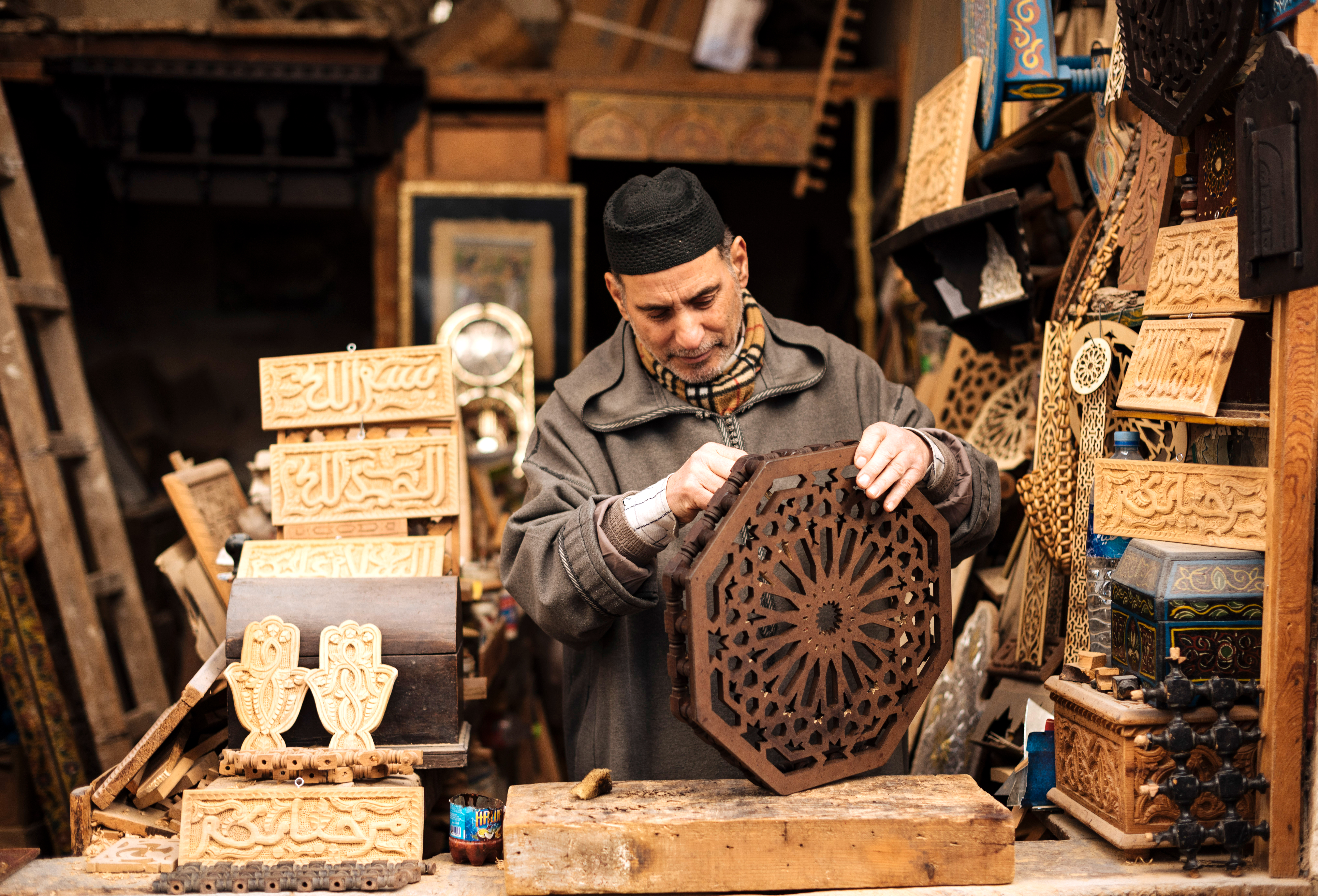 Person carving a wooden panel in a crowded craft workshop.
