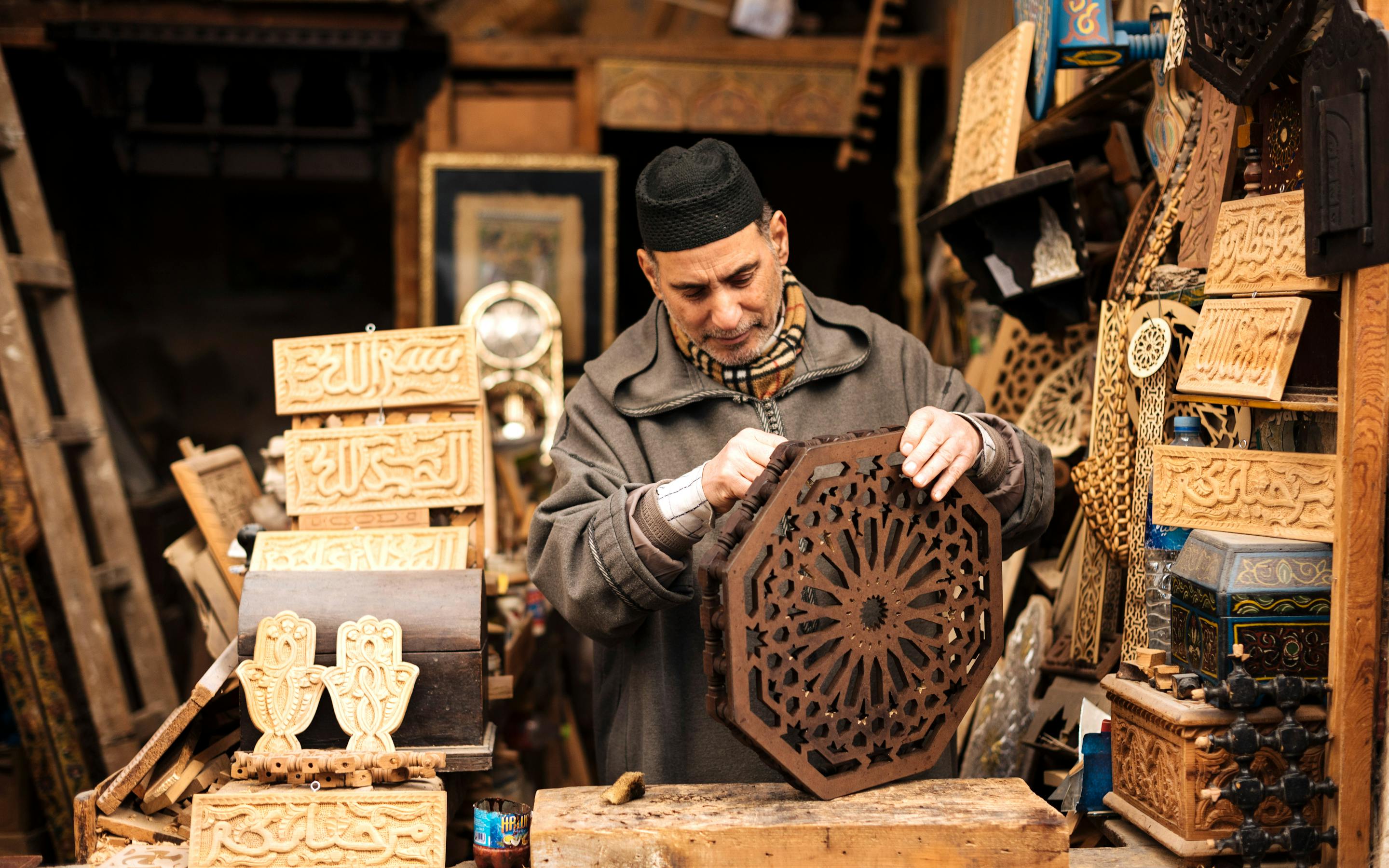 Person carving a wooden panel in a crowded craft workshop.