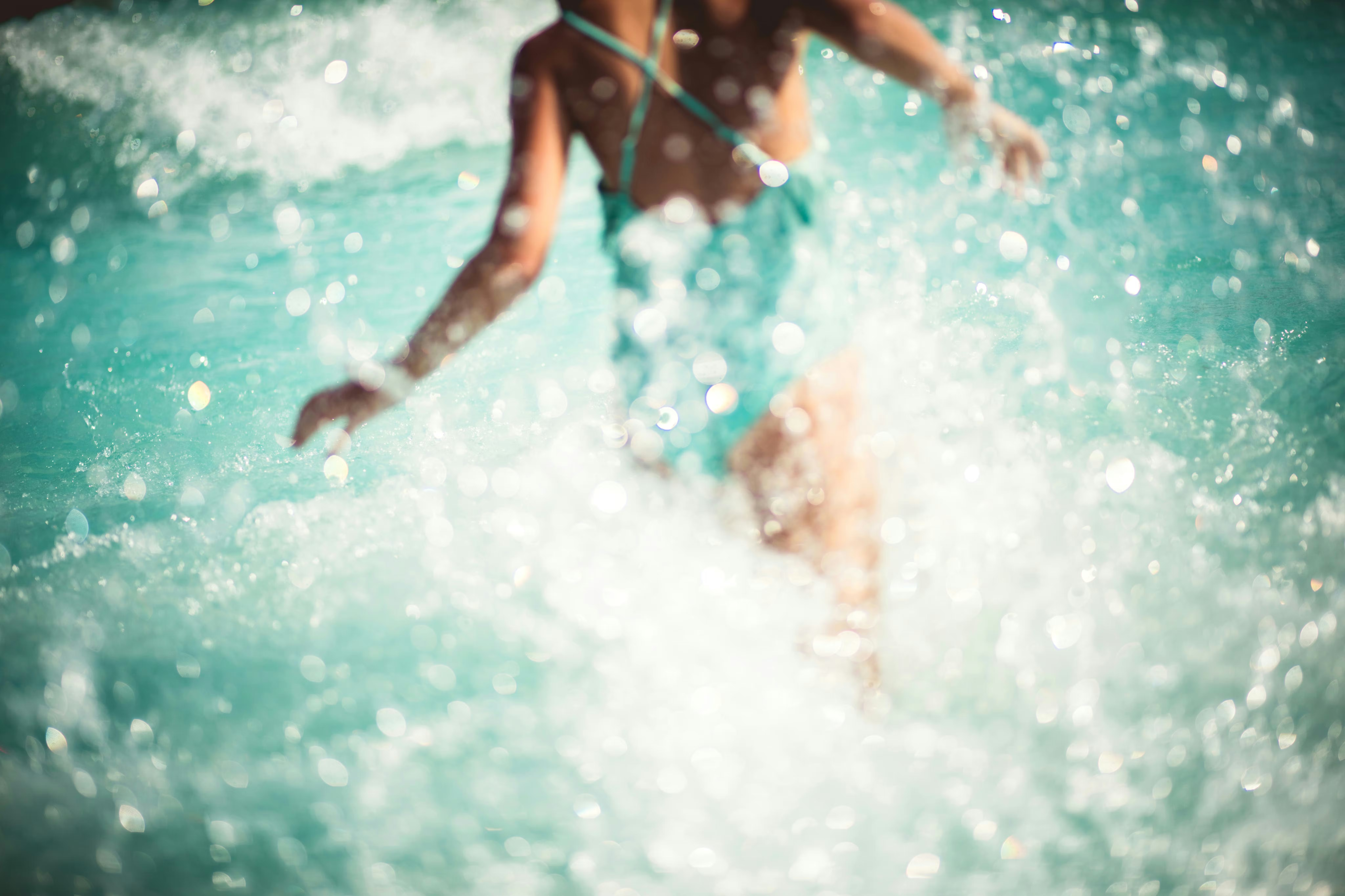 A person splashes through sunlit turquoise seawater, with bright droplets and foamy waves filling the frame.