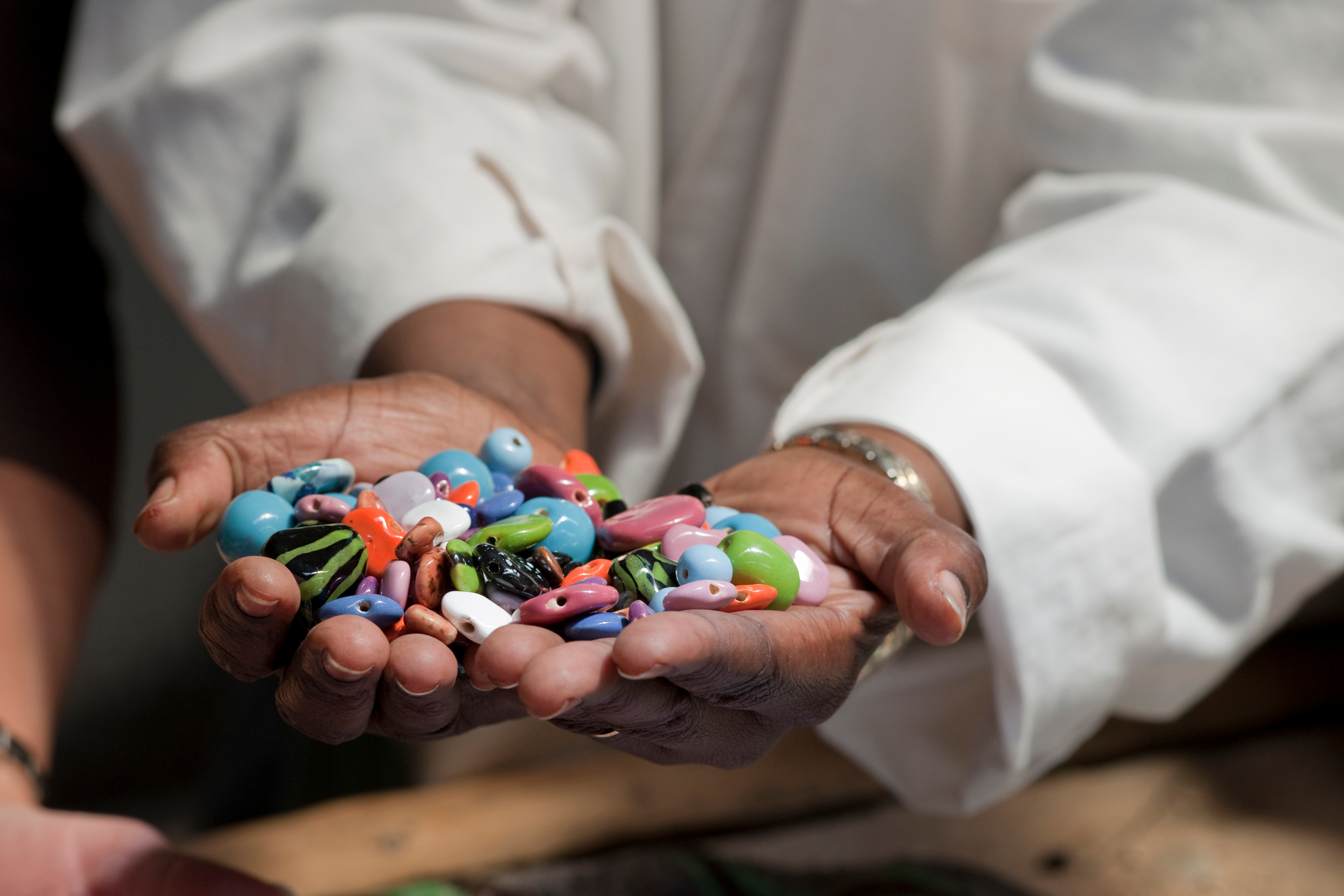 Hands hold a collection of colorful beads and small trinkets, their glossy surfaces catching soft indoor light.
