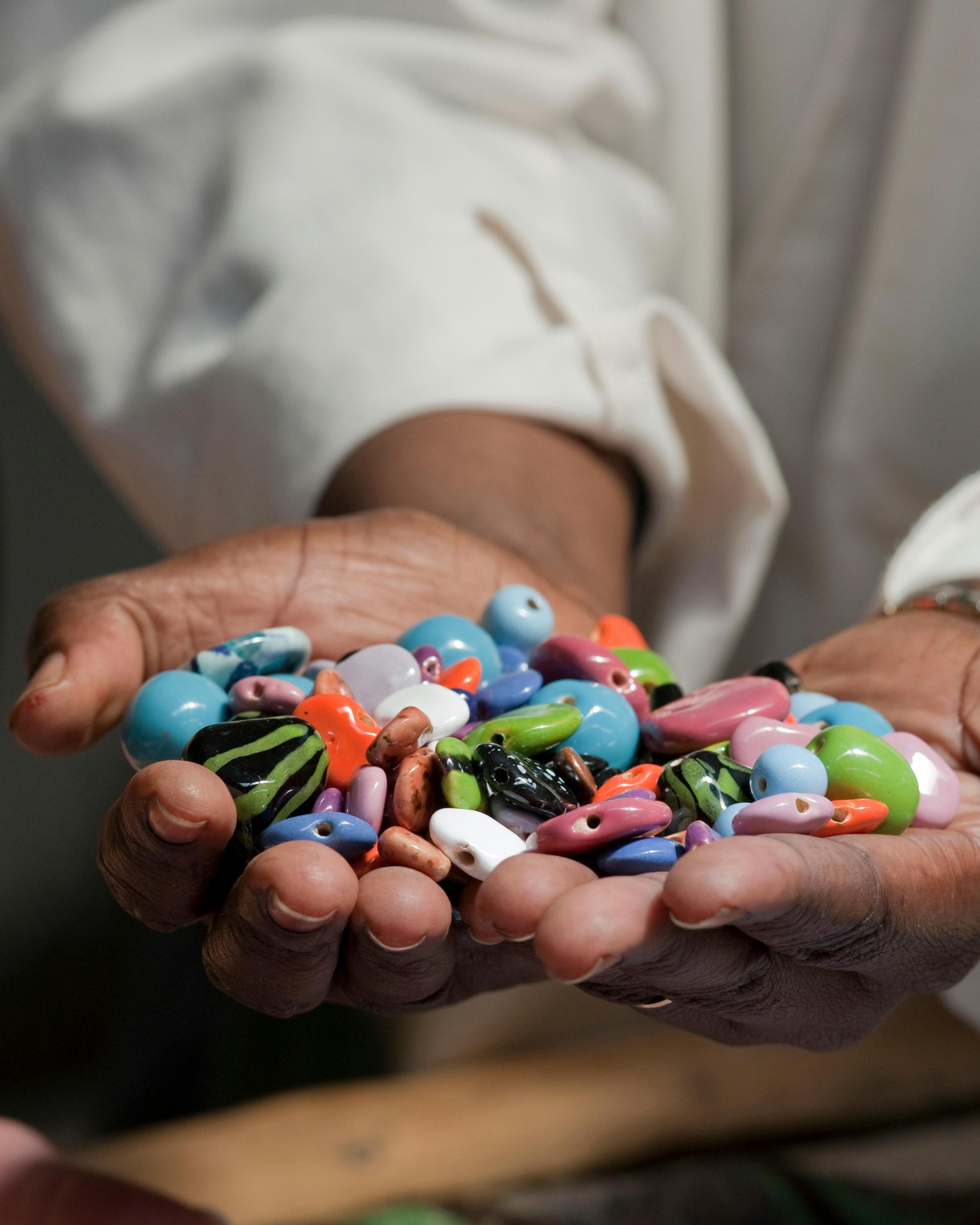Hands hold a collection of colorful beads and small trinkets, their glossy surfaces catching soft indoor light.
