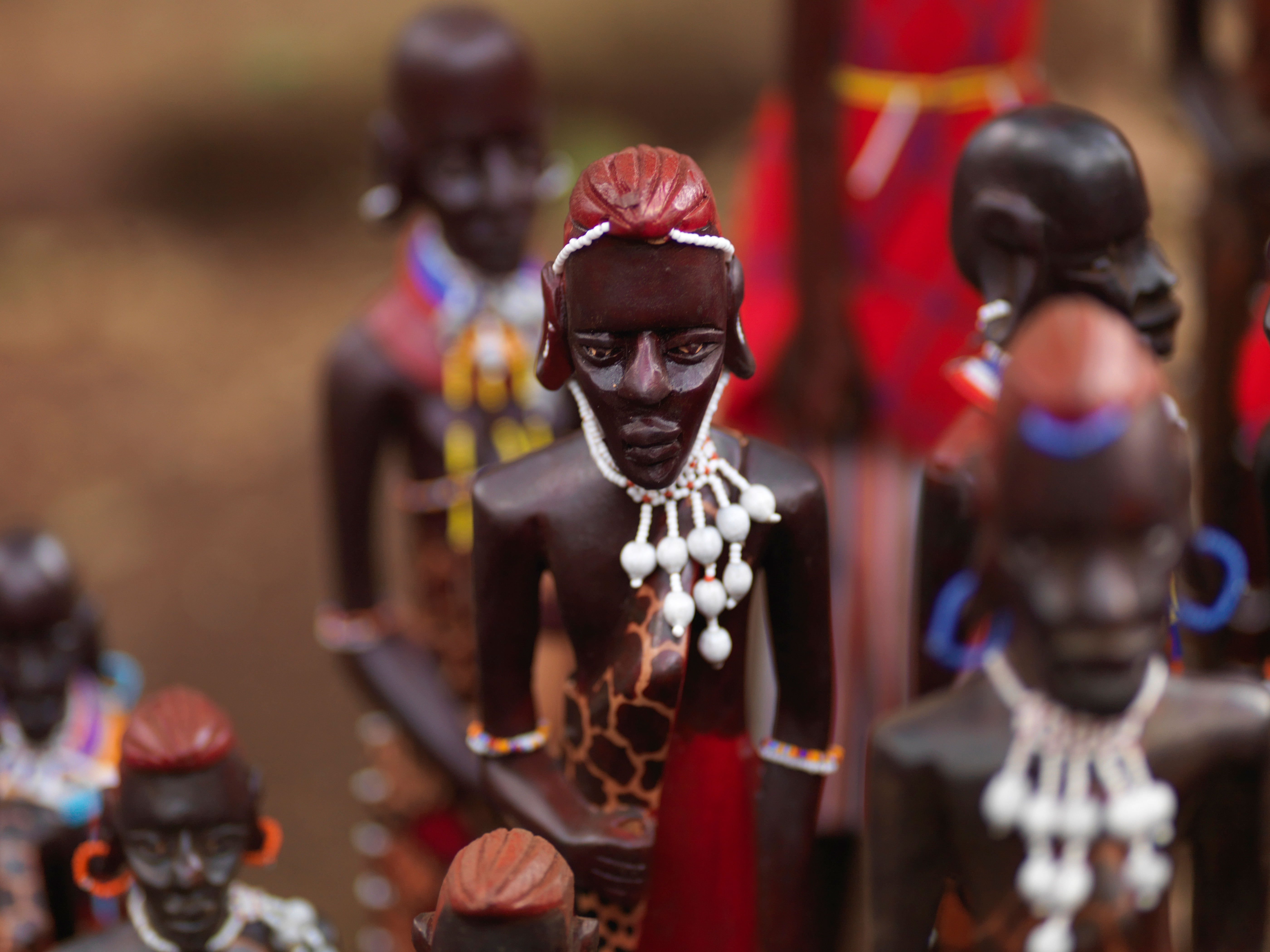 Handcrafted Maasai figurines stand in a row, their beaded jewelry and painted details shown in shallow focus.