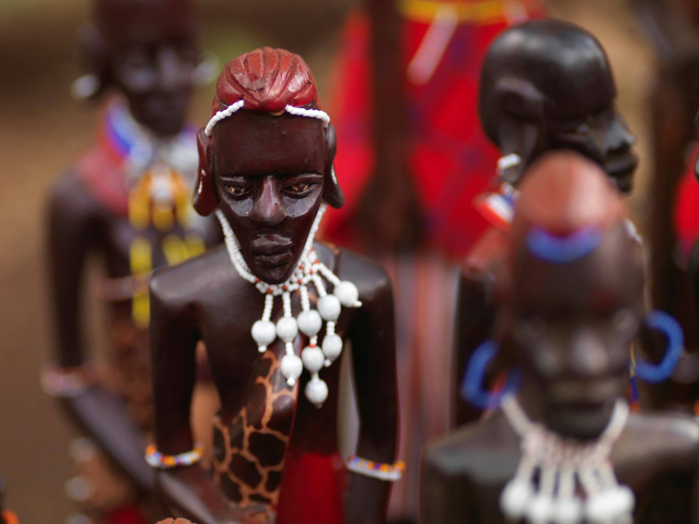 Handcrafted Maasai figurines stand in a row, their beaded jewelry and painted details shown in shallow focus.