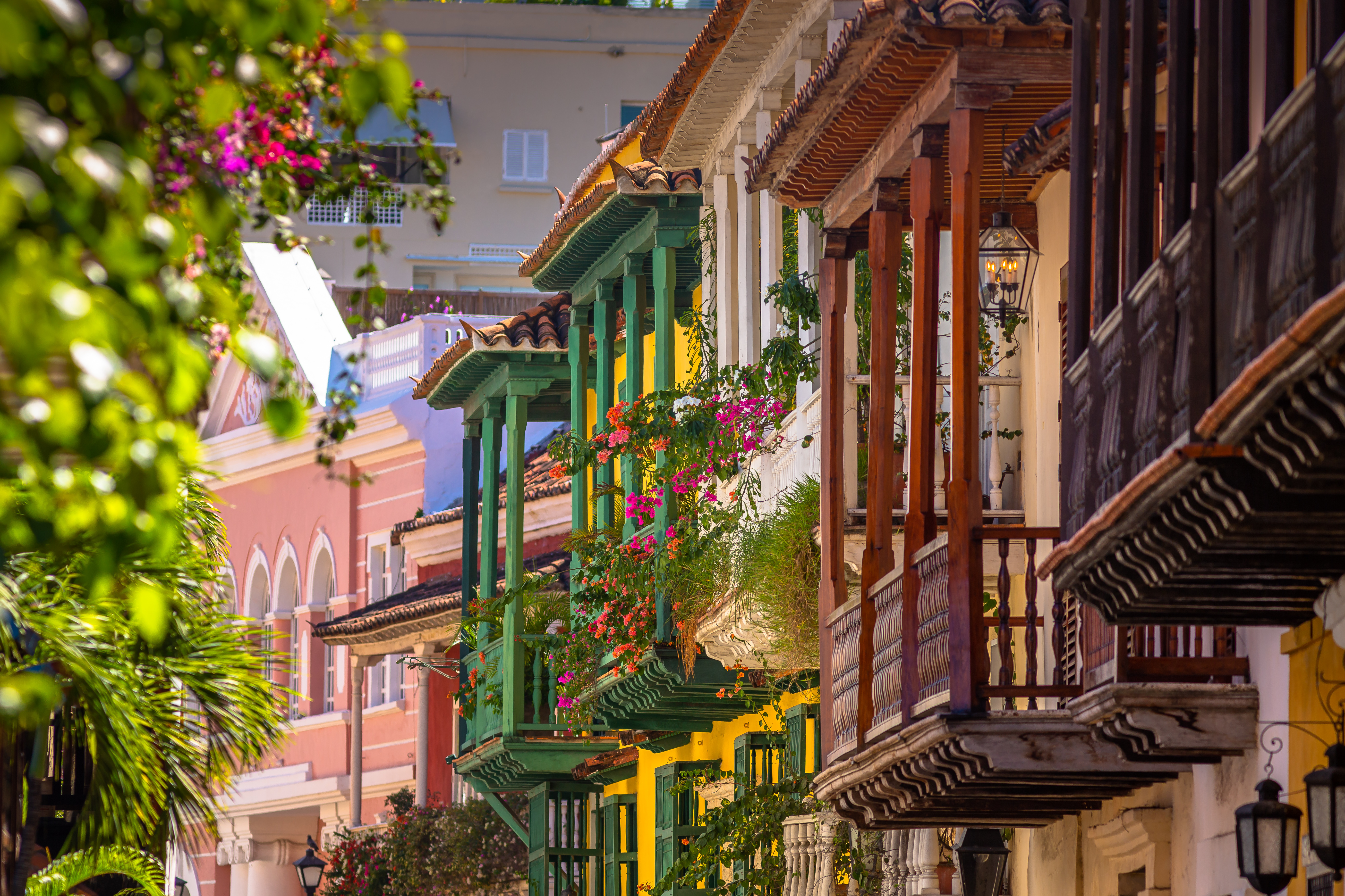 Colorful balconies draped with flowers line a narrow street in Cartagena’s old town, lit by warm afternoon sun.