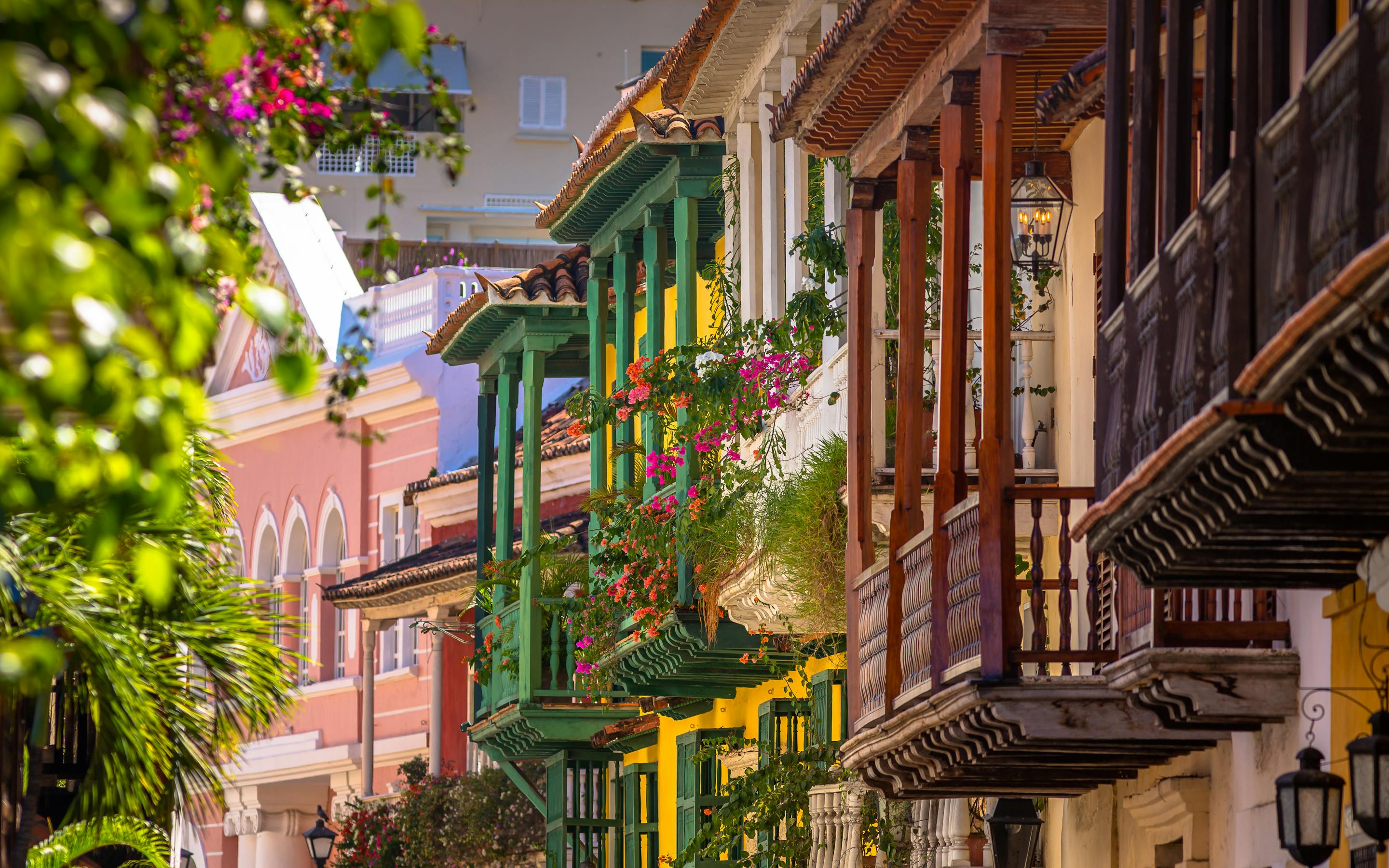 Colorful balconies draped with flowers line a narrow street in Cartagena’s old town, lit by warm afternoon sun.