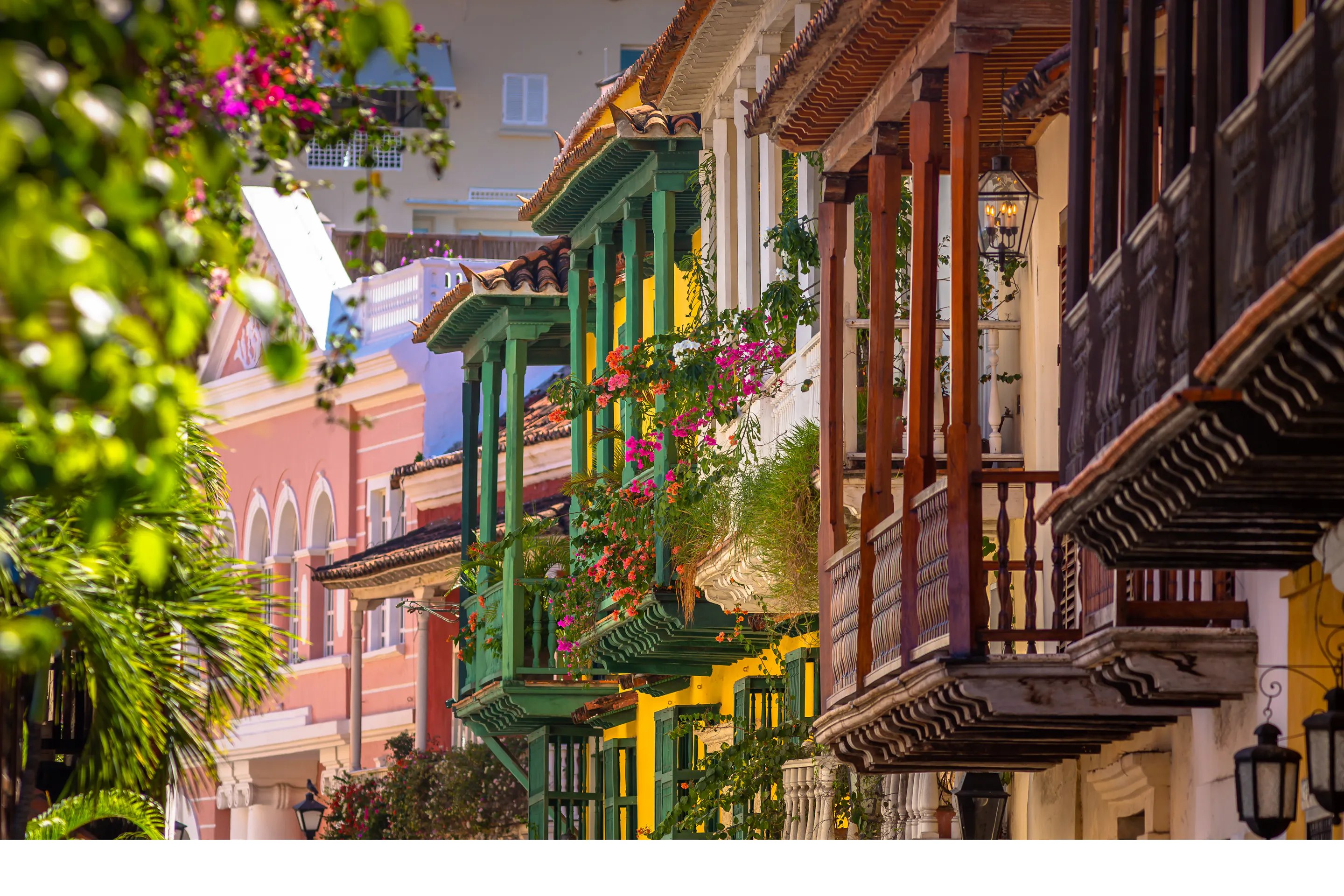 Colorful balconies draped with flowers line a narrow street in Cartagena’s old town, lit by warm afternoon sun.