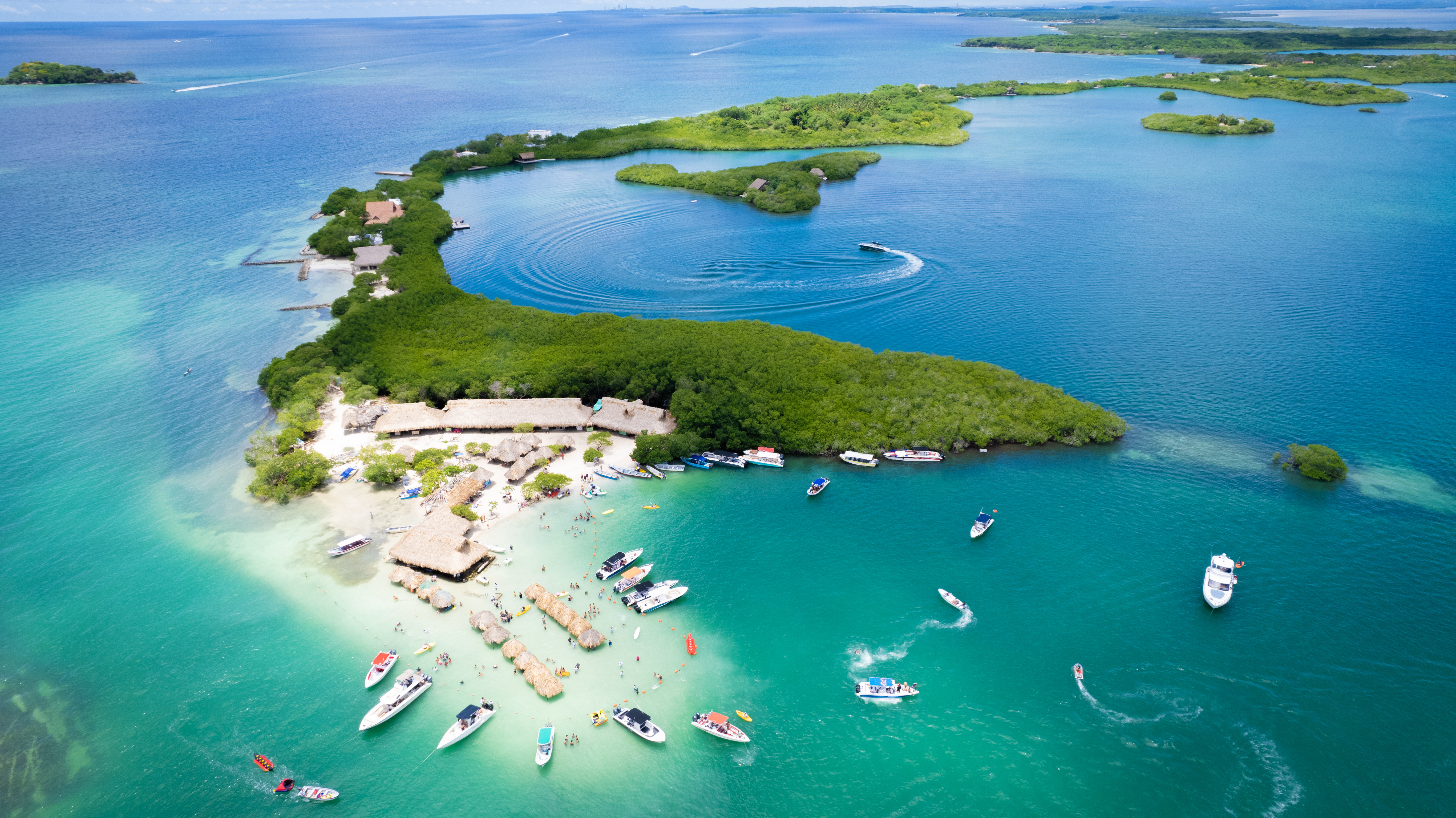 Aerial view shows bright turquoise shallows and small islands near Cartagena, with boats anchored in the lagoon.