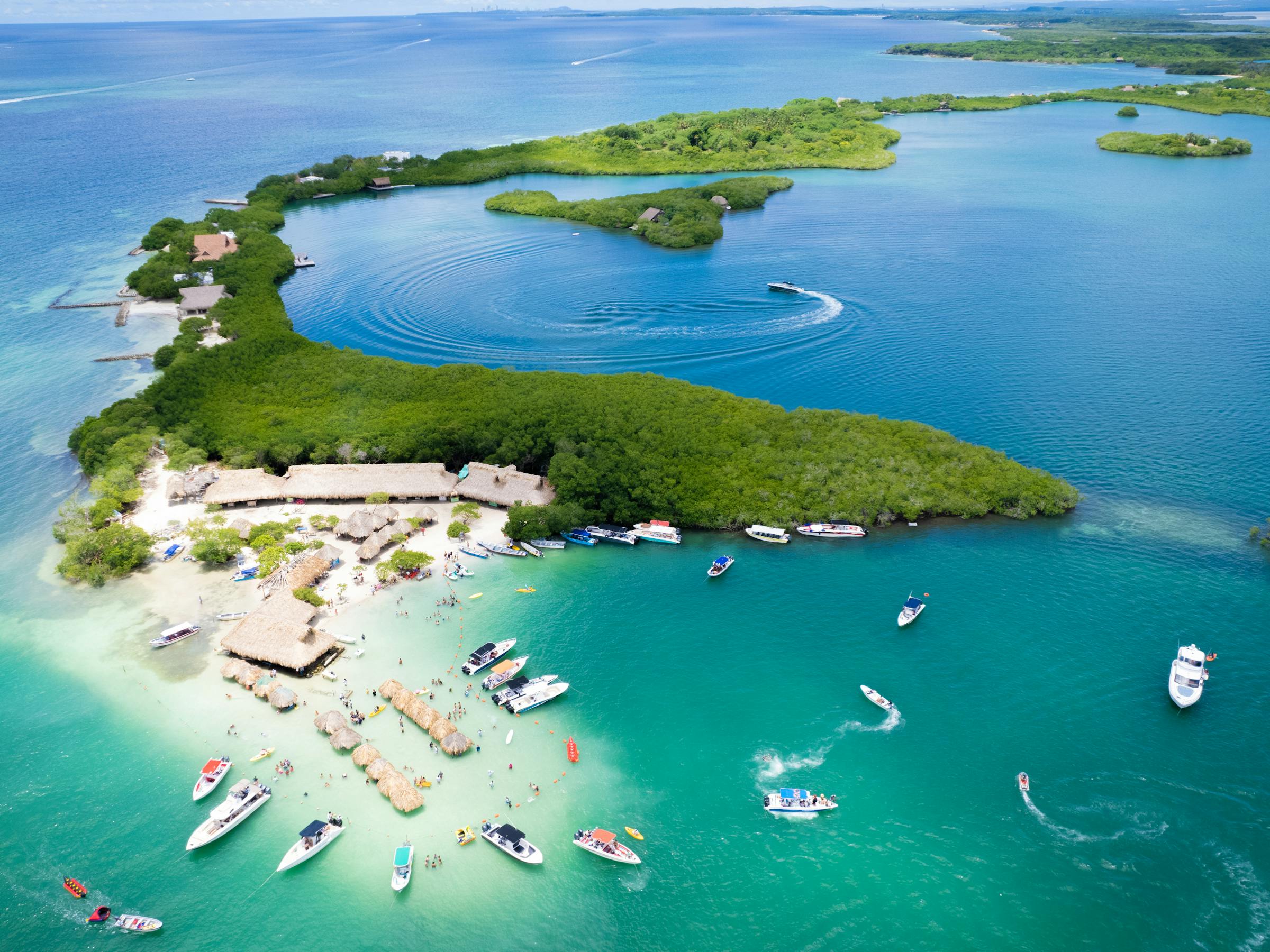 Aerial view shows bright turquoise shallows and small islands near Cartagena, with boats anchored in the lagoon.