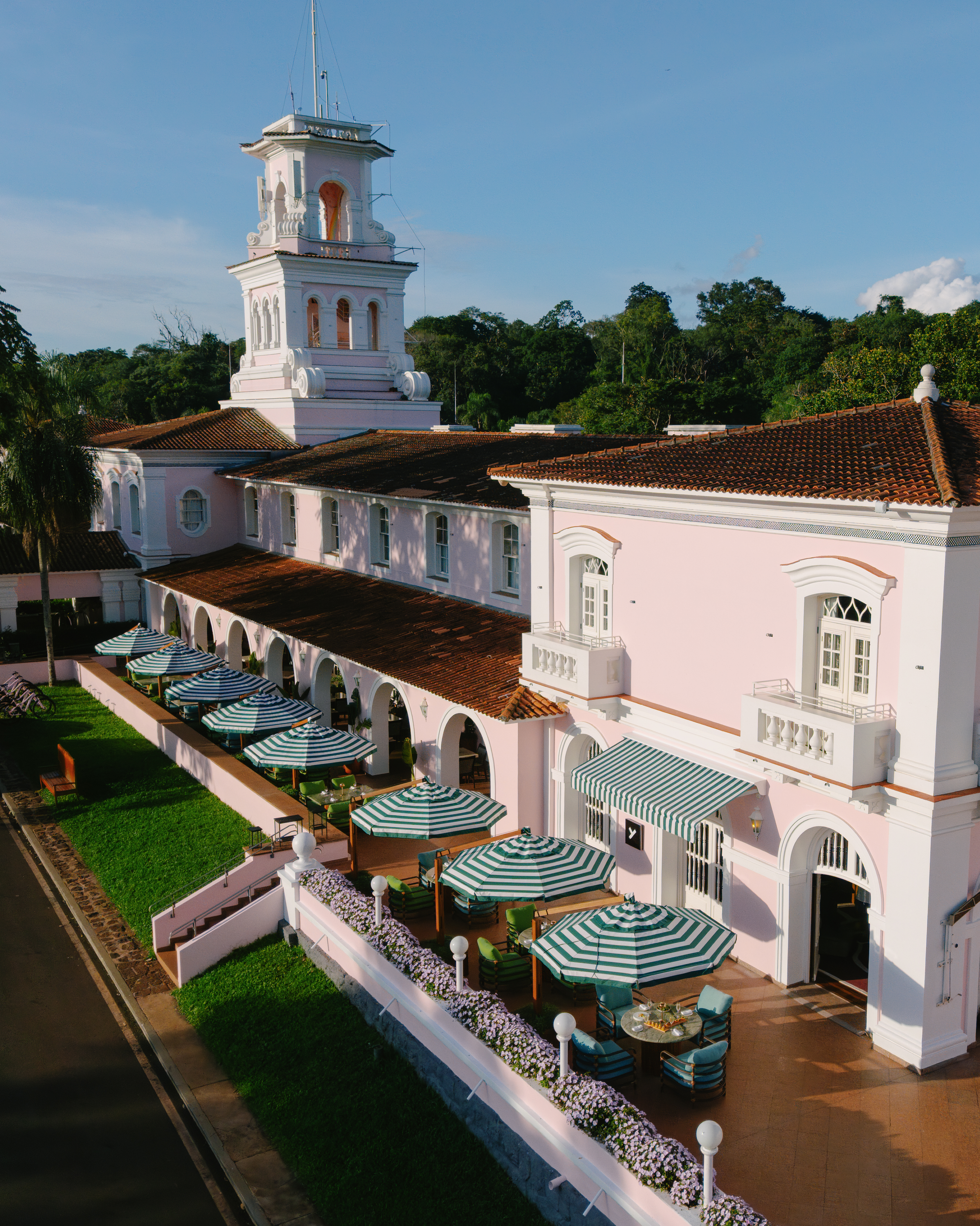 Outdoor tables line a white colonnade at Hotel das Cataratas, with green awnings and manicured lawns beyond.