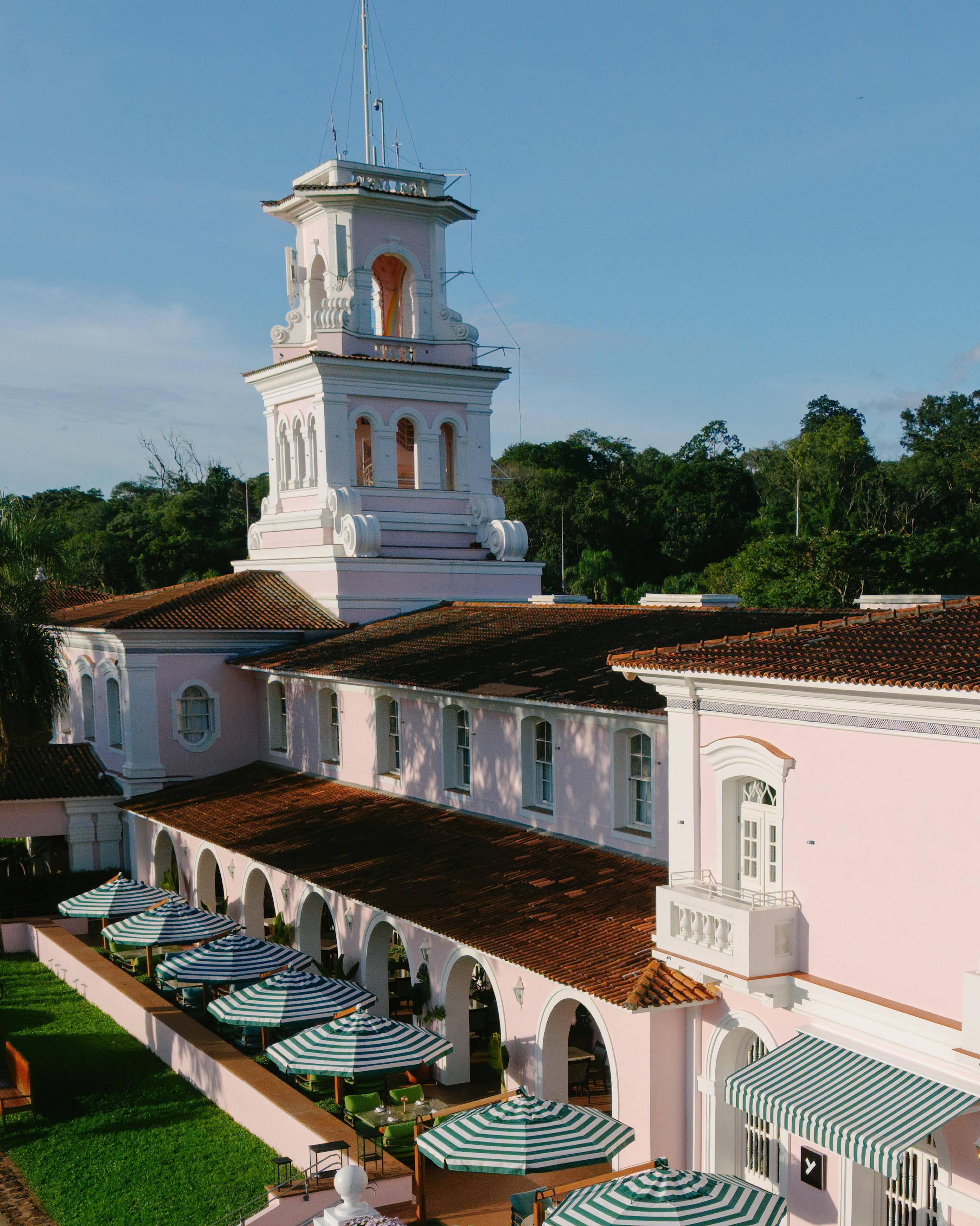 Outdoor tables line a white colonnade at Hotel das Cataratas, with green awnings and manicured lawns beyond.