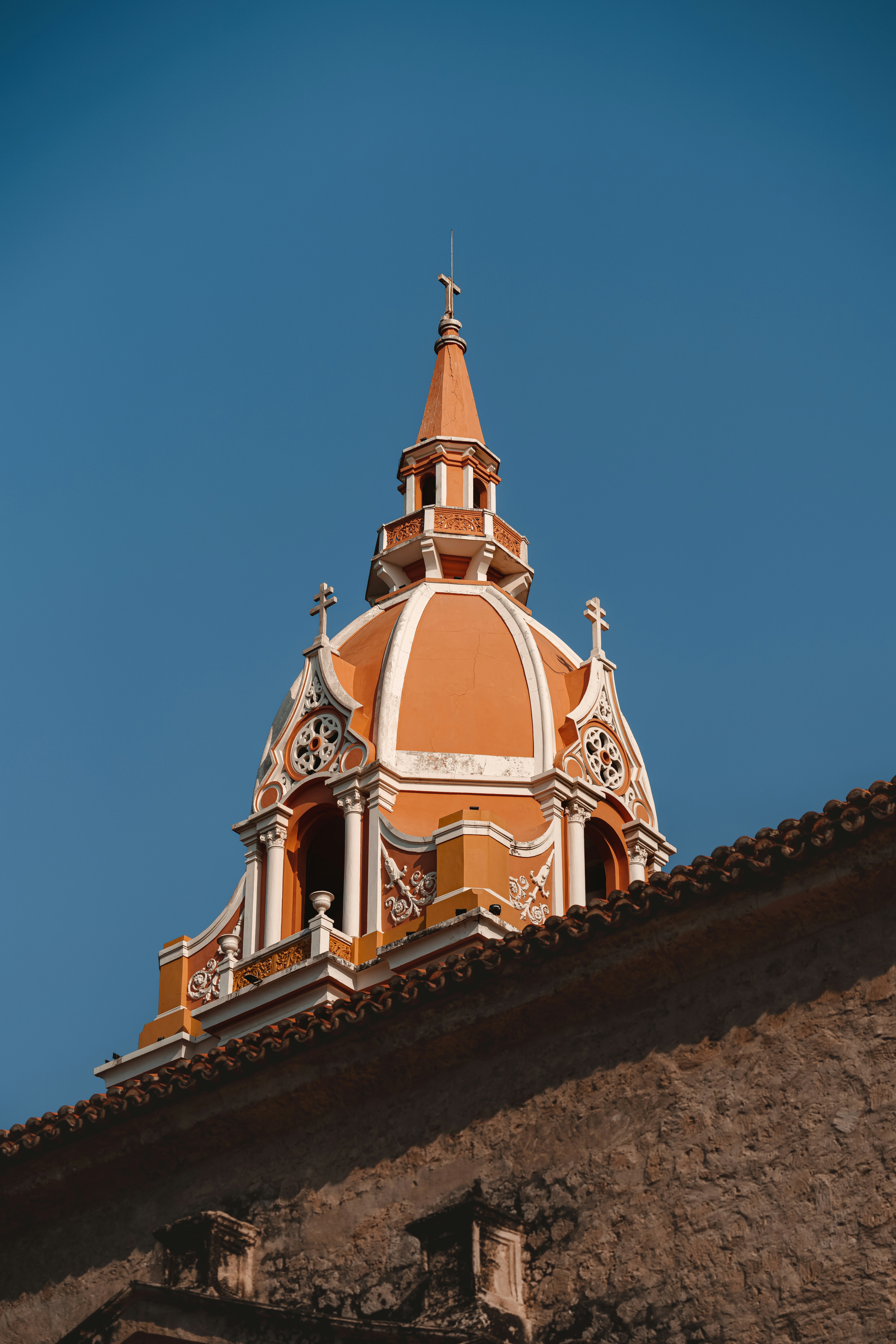 A close-up view of the Cartagena cathedral dome rises above tiled roofs, set against a clear blue sky behind.