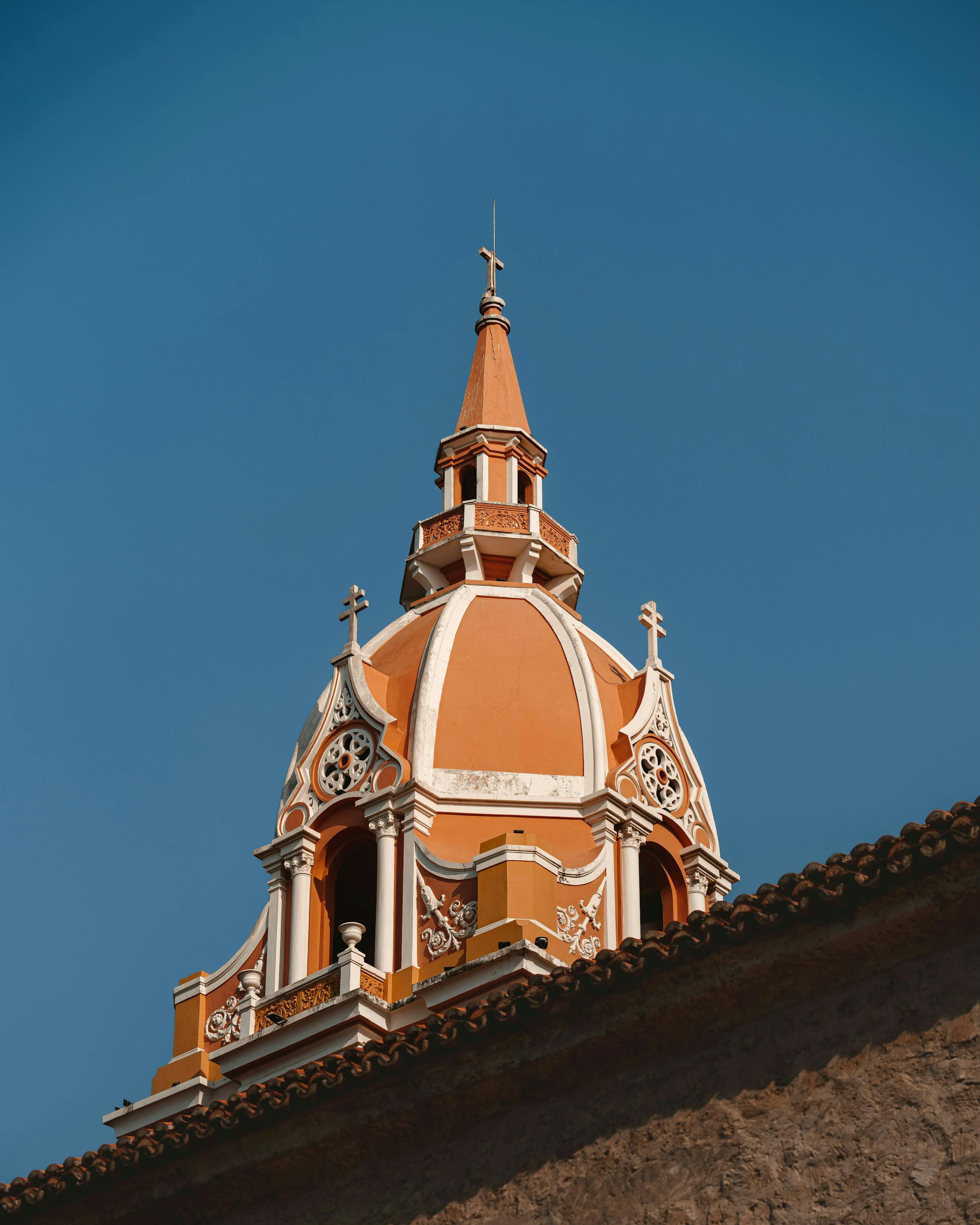 A close-up view of the Cartagena cathedral dome rises above tiled roofs, set against a clear blue sky behind.