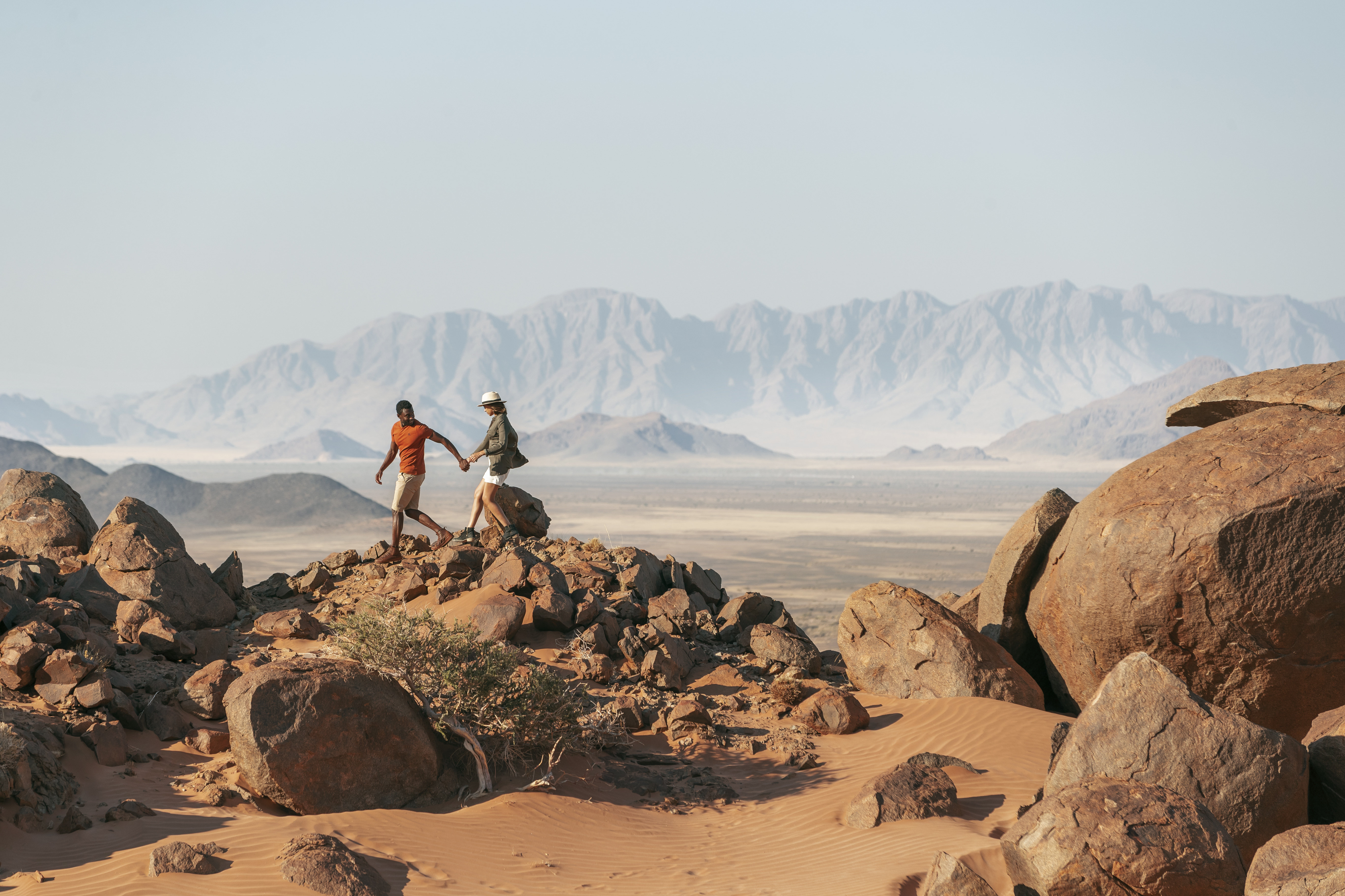 two people holding hands and walking in Namibia's desert rocks