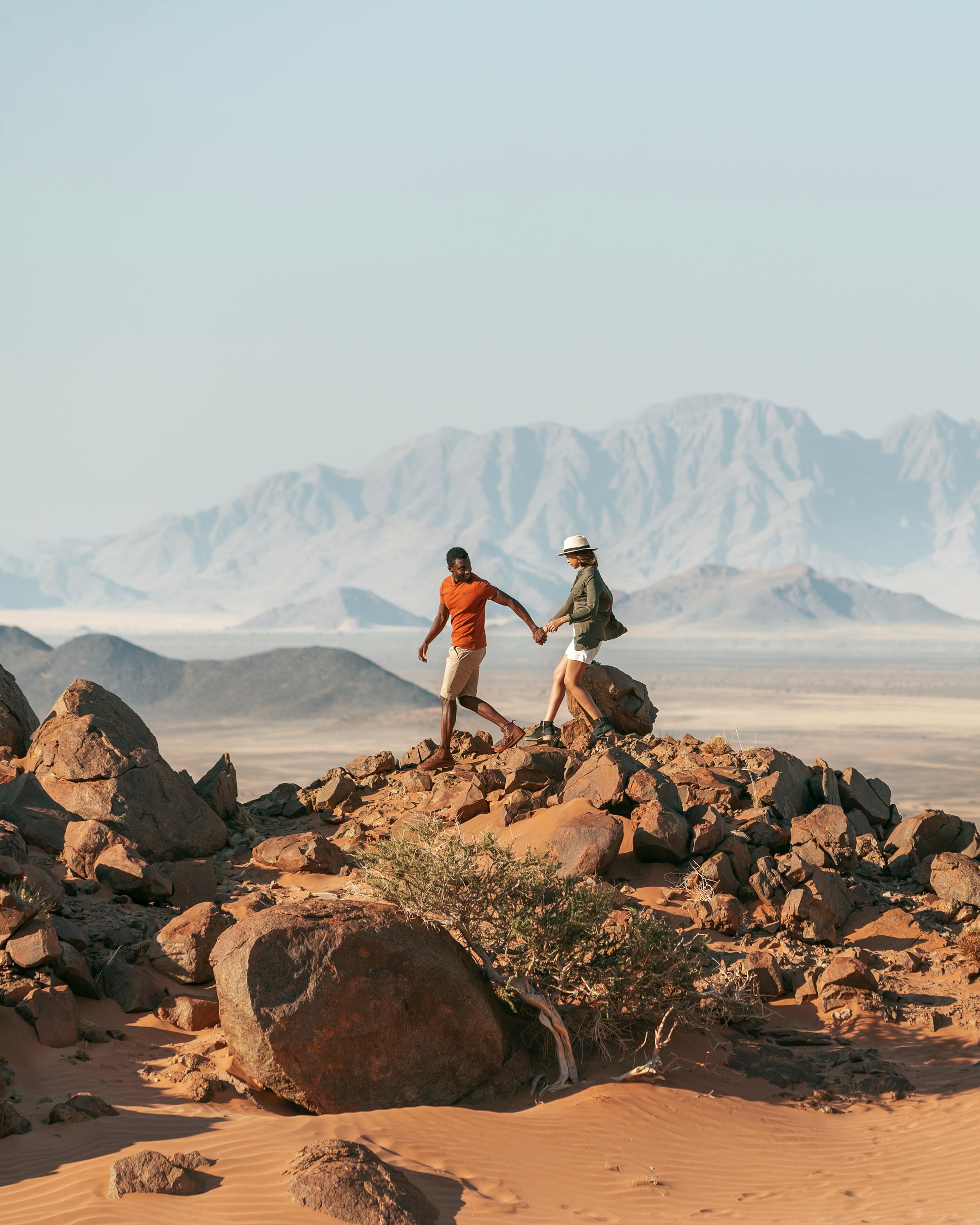 two people holding hands and walking in Namibia's desert rocks