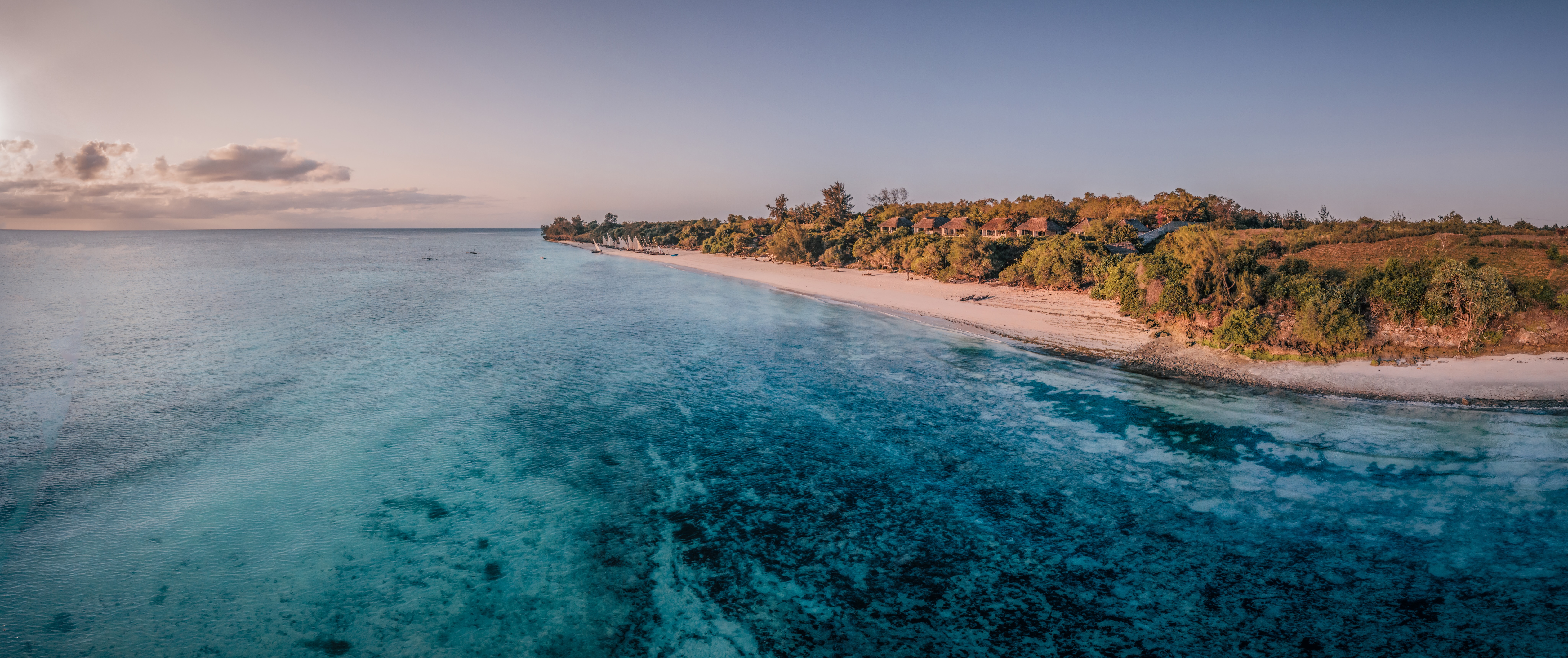 Aerial panorama of coastline at sunset, with warm light on the water and layered clouds on the horizon in the distance.