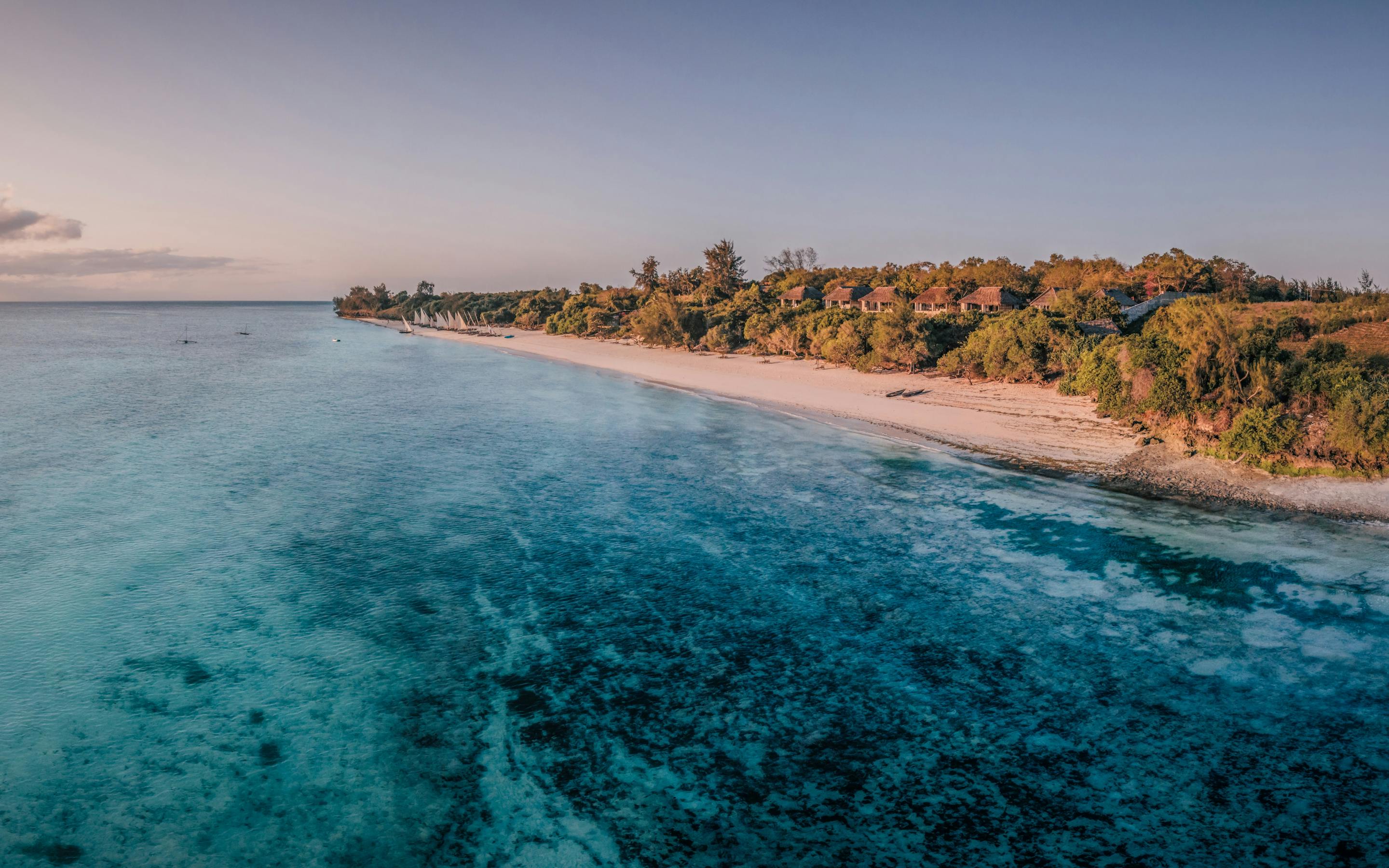 Aerial panorama of coastline at sunset, with warm light on the water and layered clouds on the horizon in the distance.