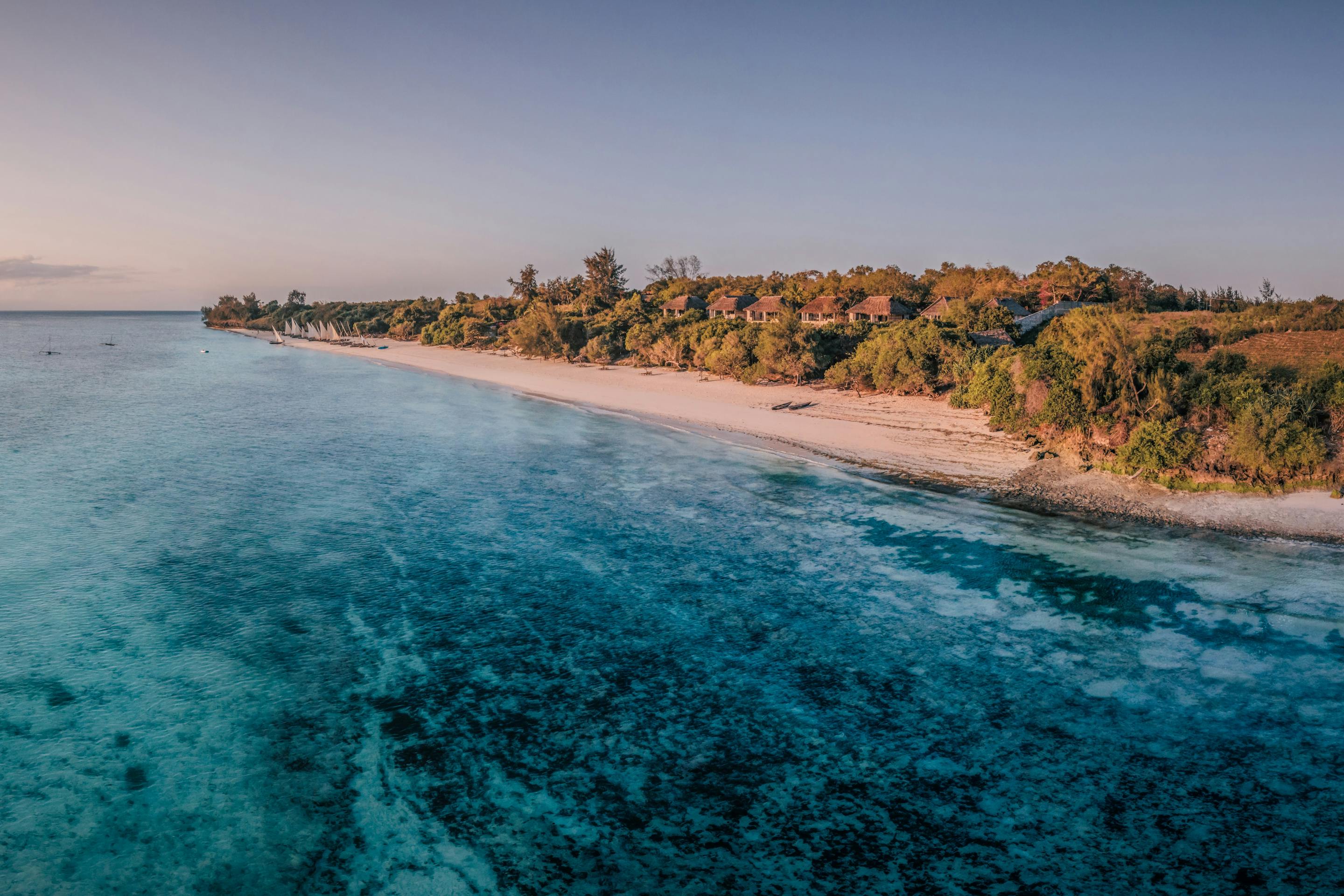 Aerial panorama of coastline at sunset, with warm light on the water and layered clouds on the horizon in the distance.