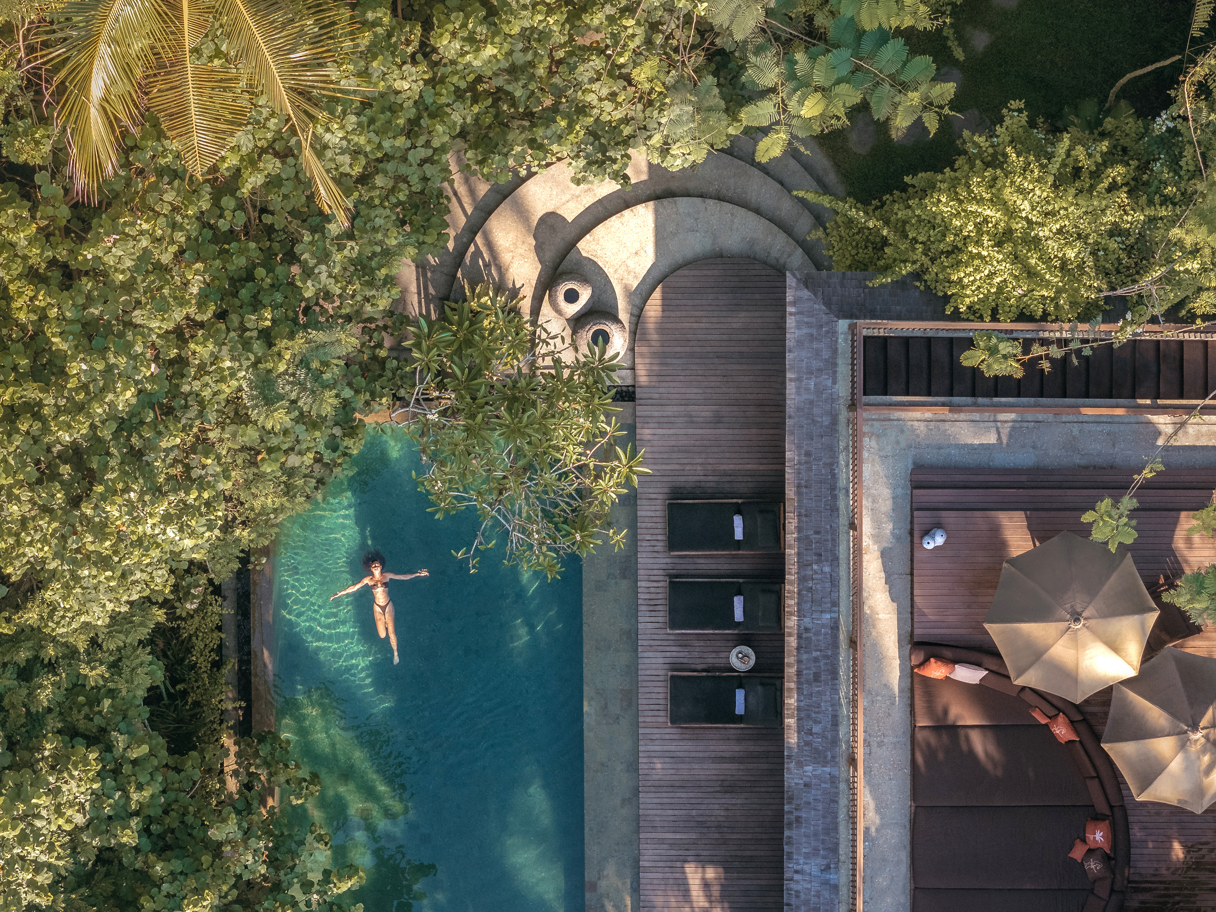 Aerial view of a pool beside a modern building surrounded by trees.