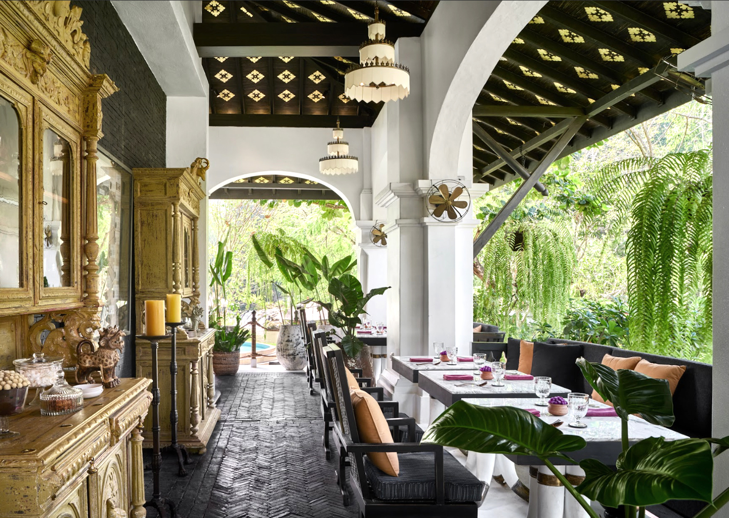 Open-air restaurant with arched columns, set tables, and lush greenery outside.