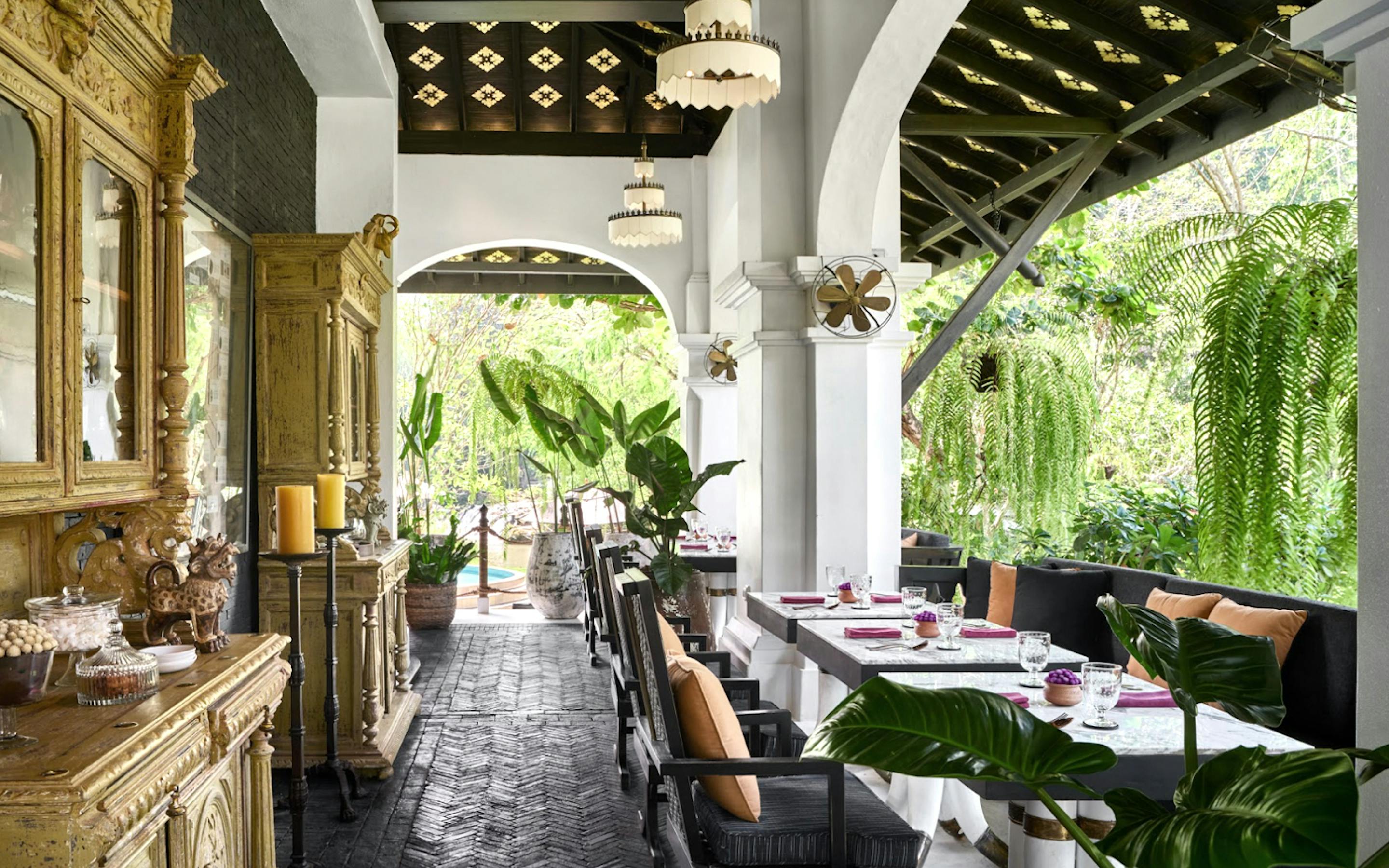 Open-air restaurant with arched columns, set tables, and lush greenery outside.