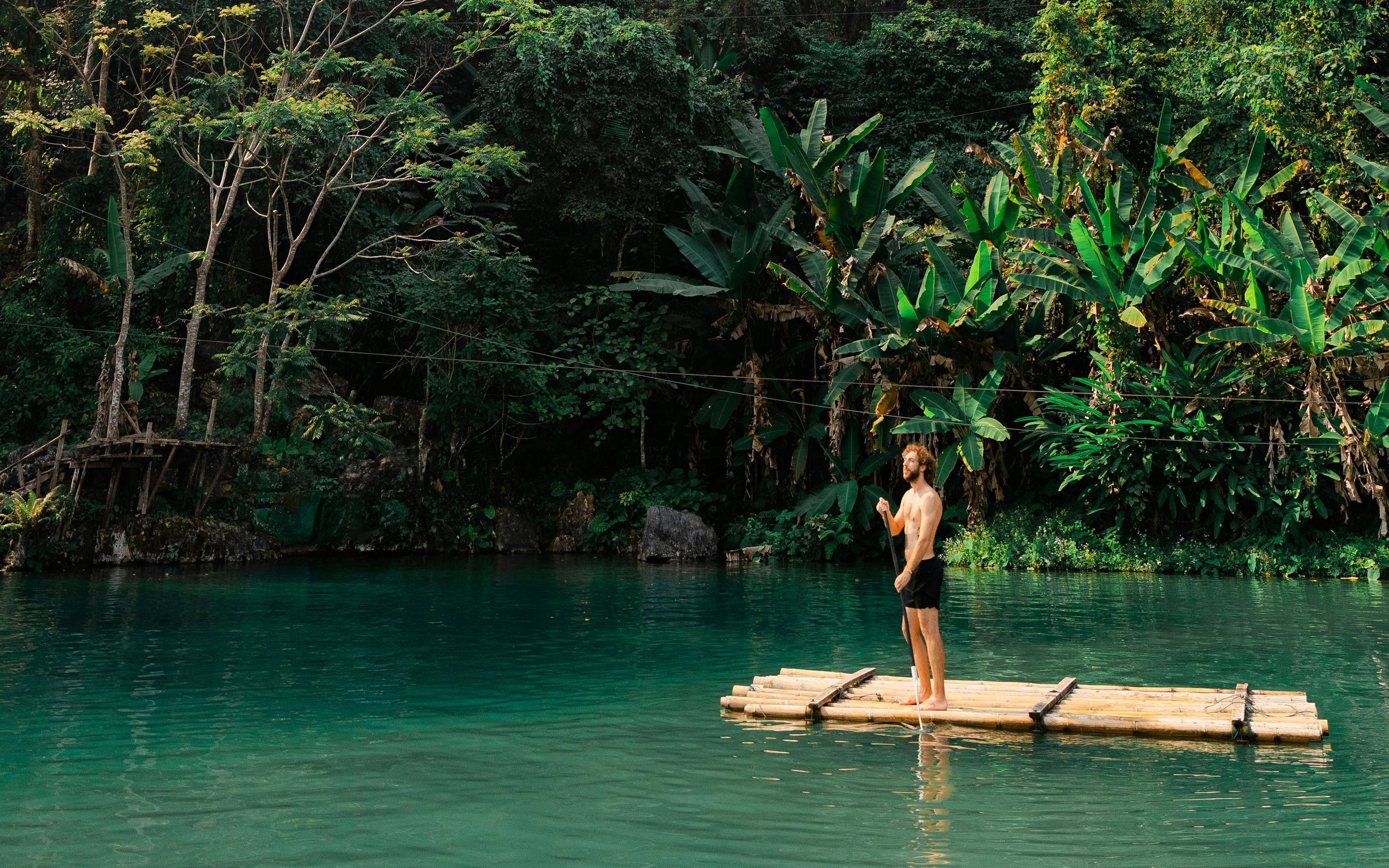 Person on a small raft floats on turquoise water beneath forested cliffs.