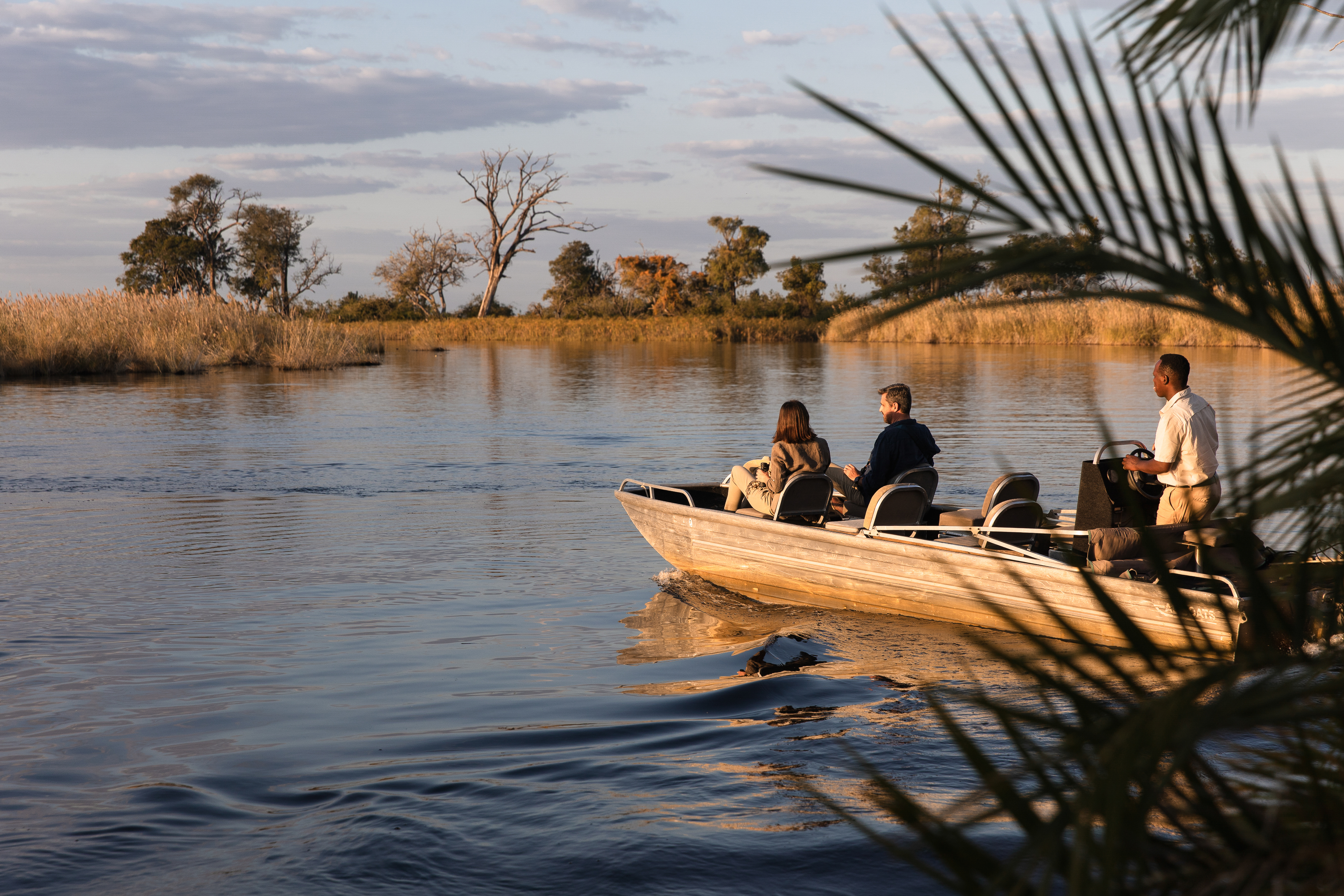 A small boat glides along a calm delta channel, with reeds and open water reflecting golden evening light.