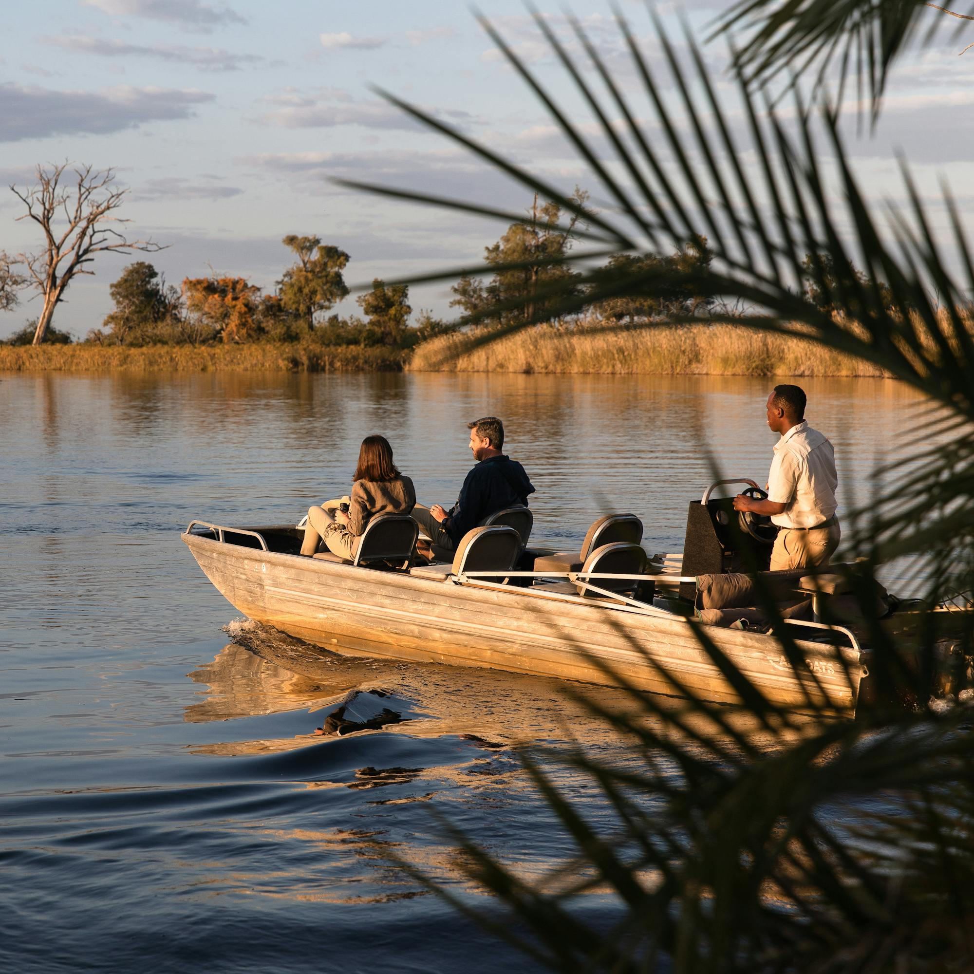 A small boat glides along a calm delta channel, with reeds and open water reflecting golden evening light.