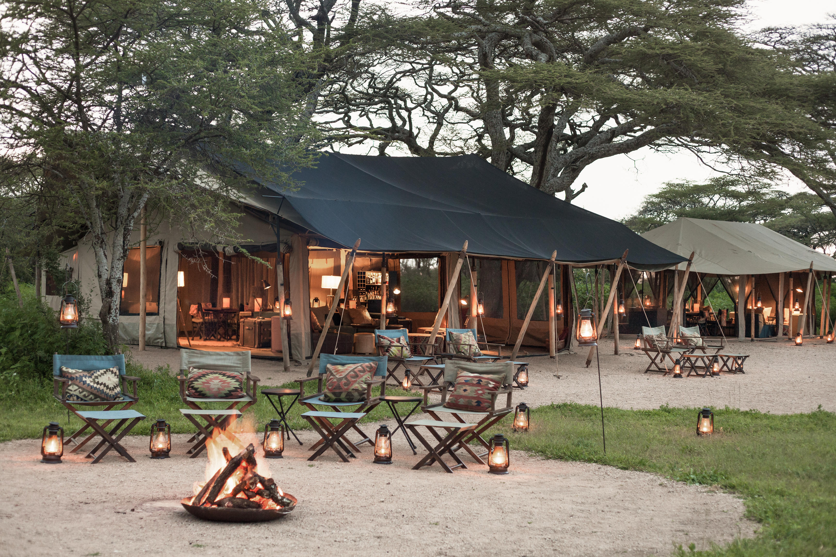Canvas tents and a shaded lounge area sit on open plains, with wooden decks and chairs facing outward.